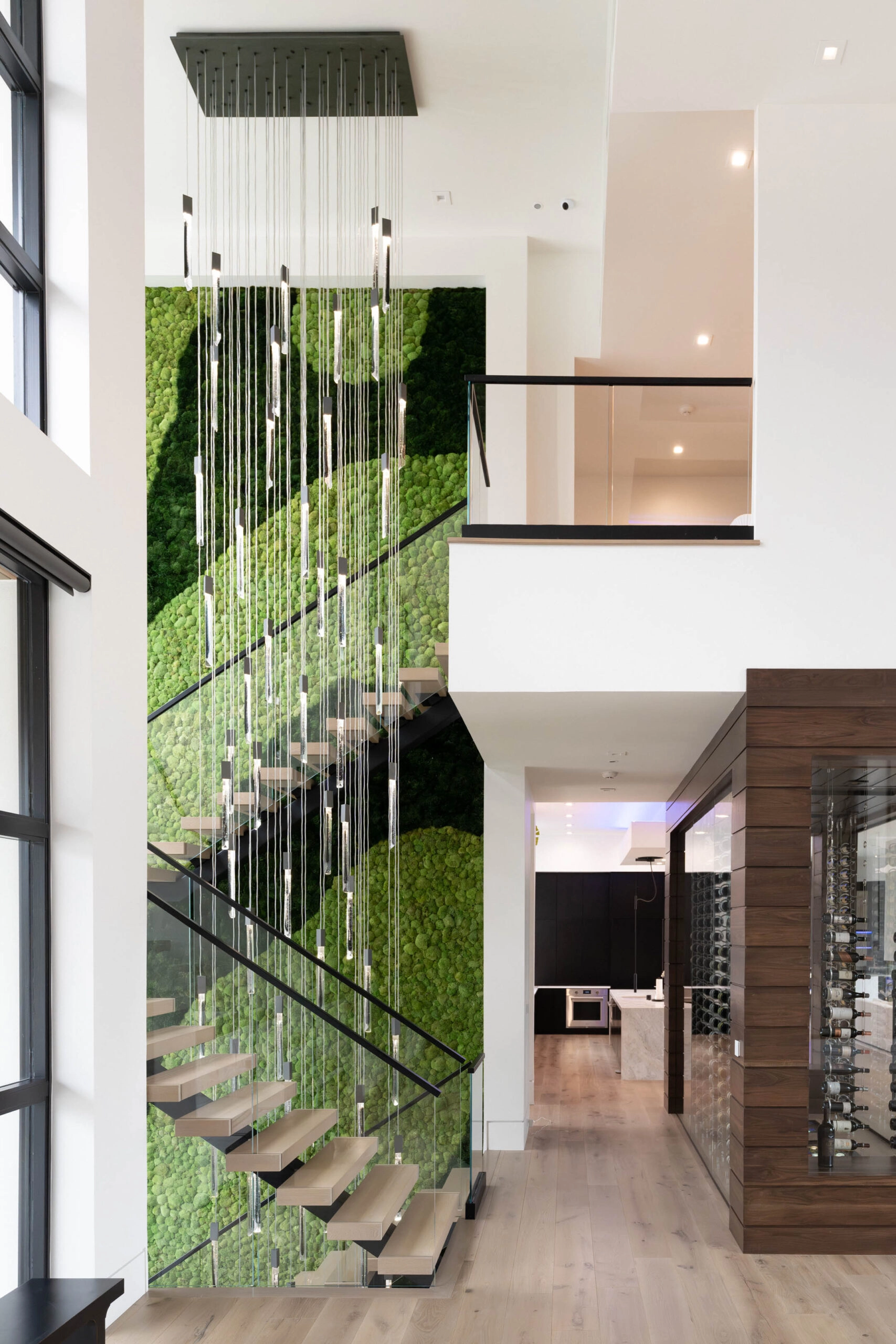 A floating stair crosses a green wall beneath a cascade of slender pendants