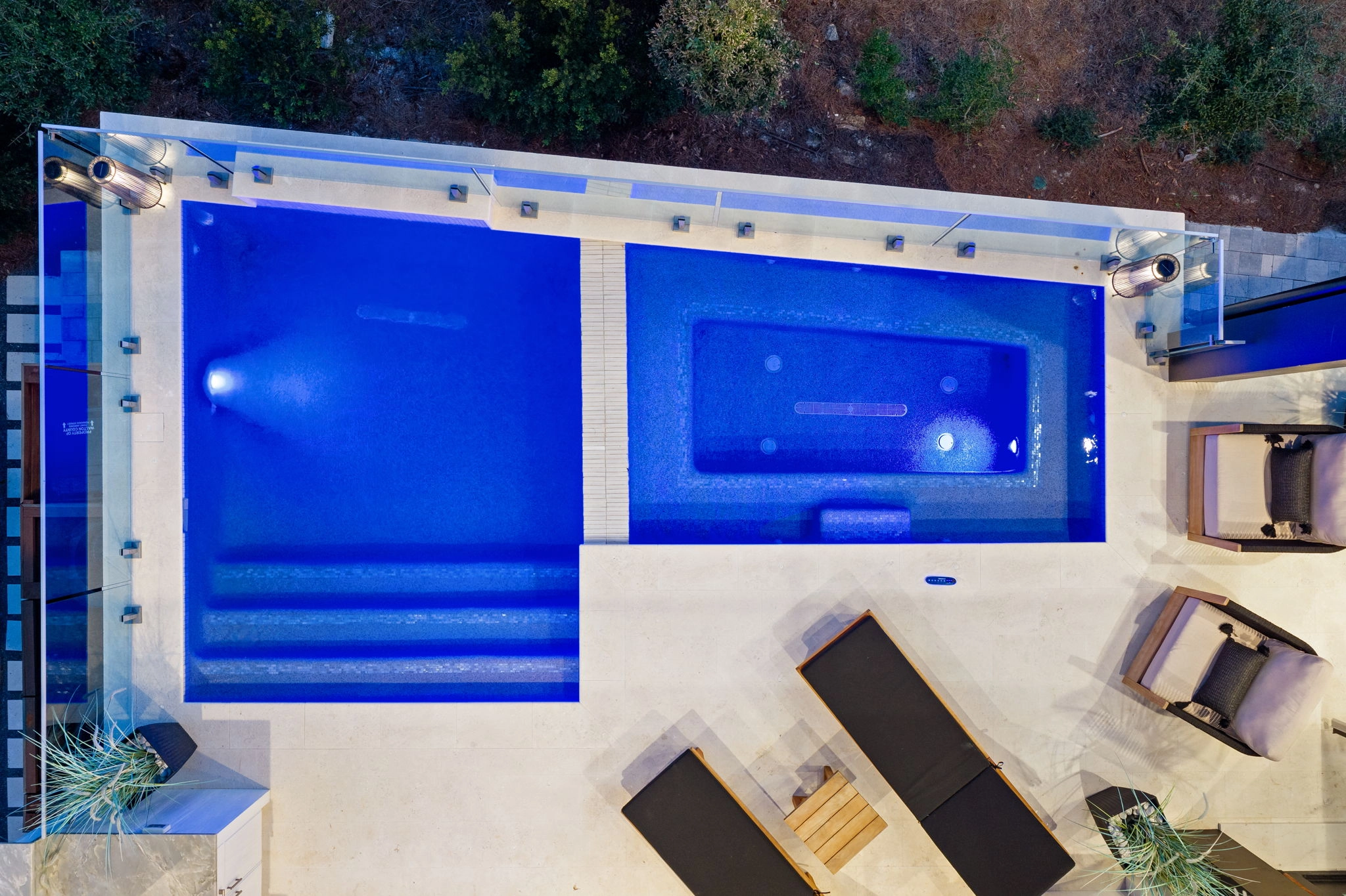 Glass railing edges a lit pool terrace seen from above after dark