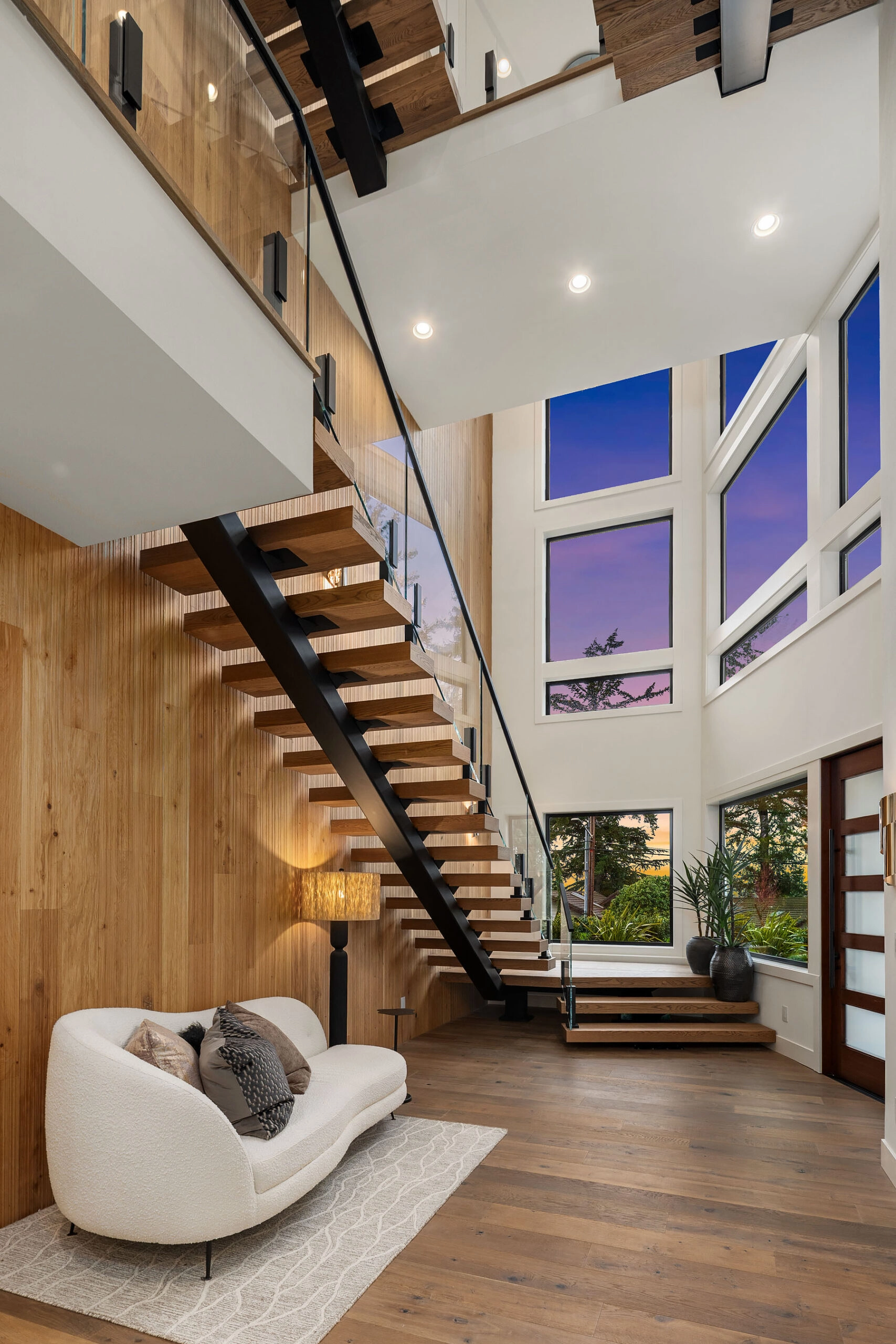 Floating stair and glass railing anchor a great room lined in wood planks