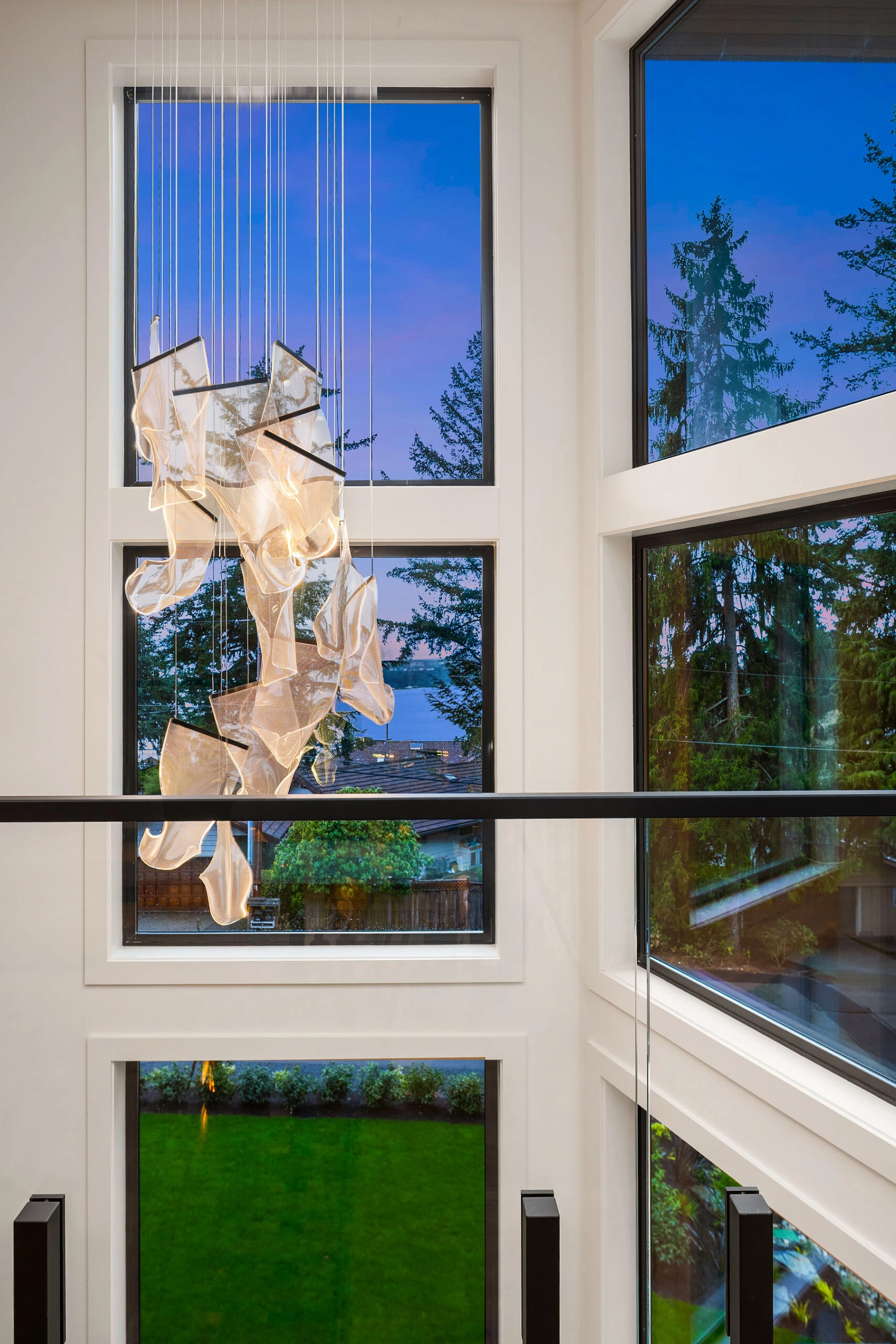 Glass railing borders a two-story window wall hung with a sculptural chandelier