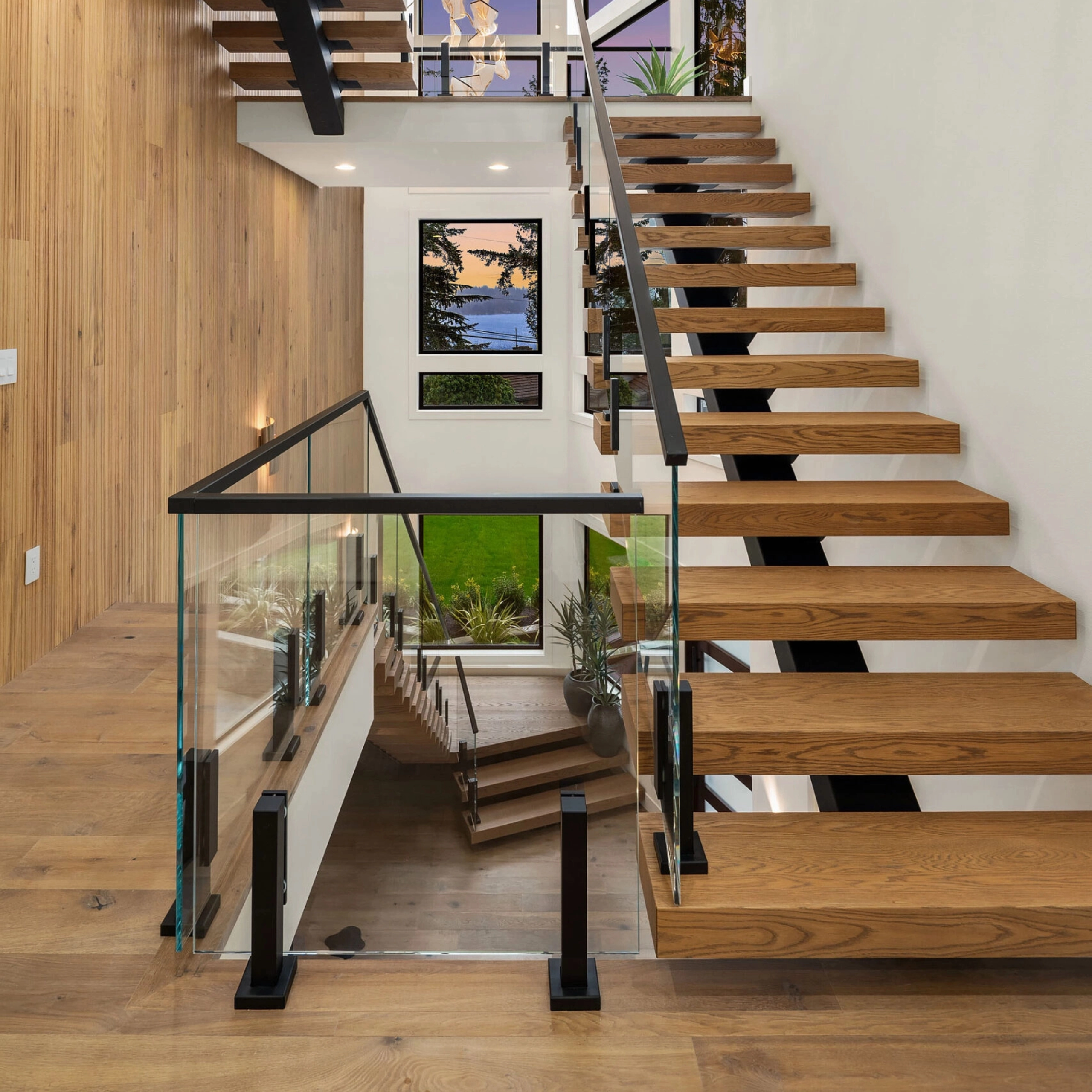 Glass panels on slim black mounts border a wood-tread stair and open landing