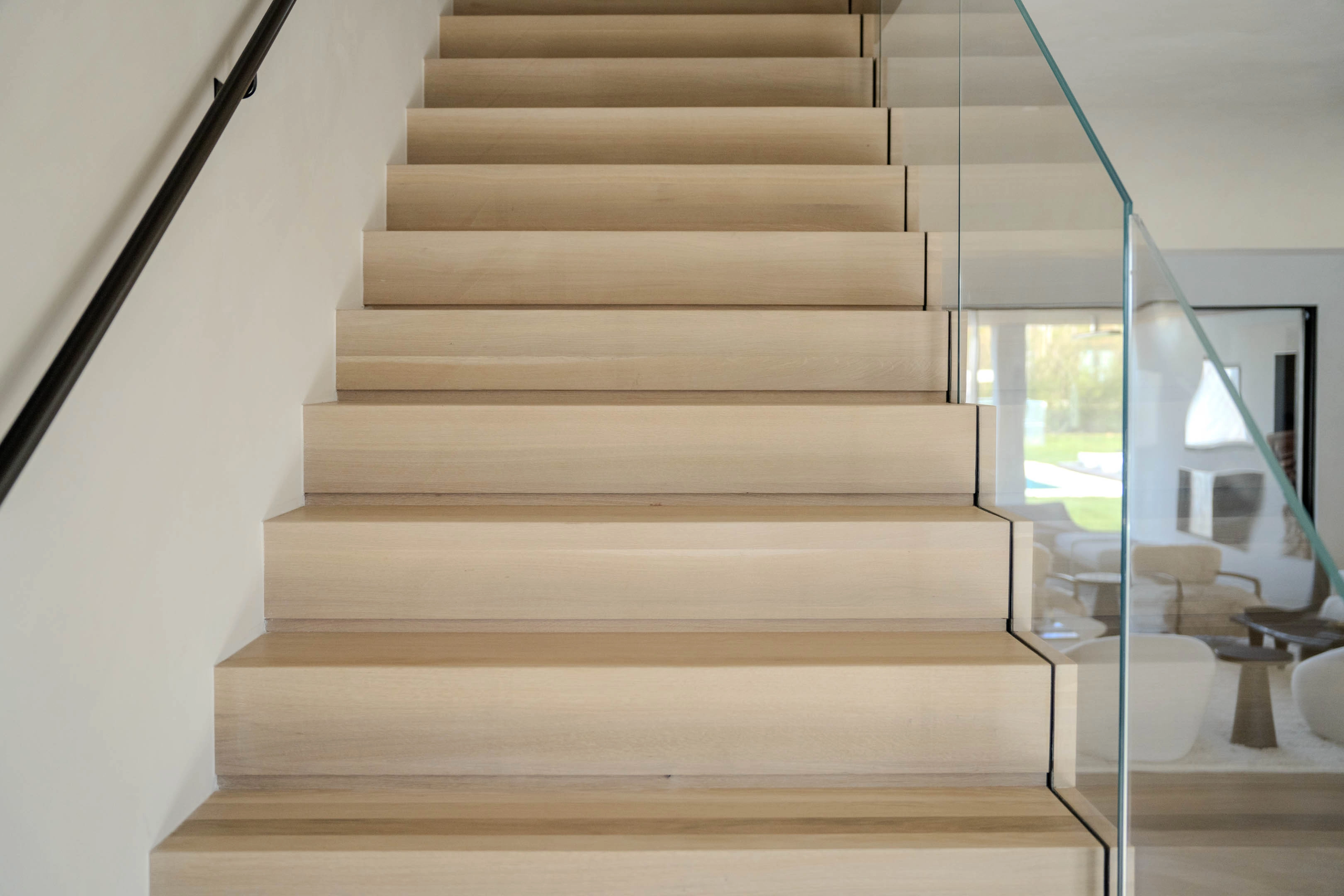 Pale treads climb between a black handrail and a clear glass panel