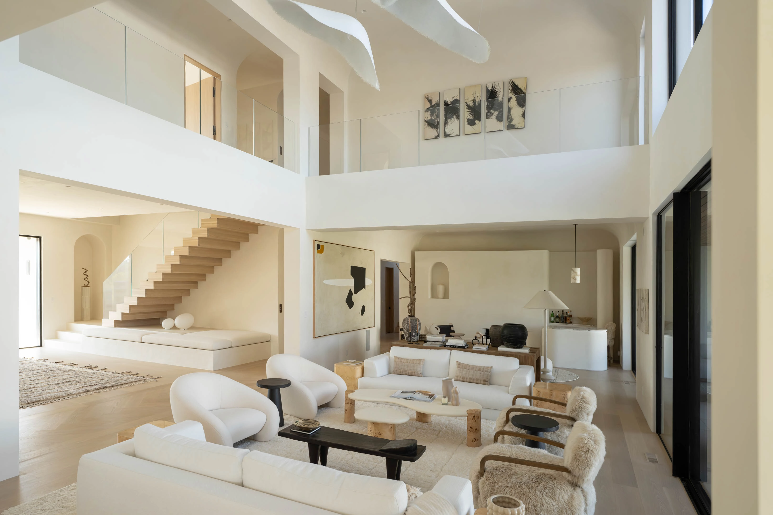 A pale double-height living room with a stair crossing the upper level
