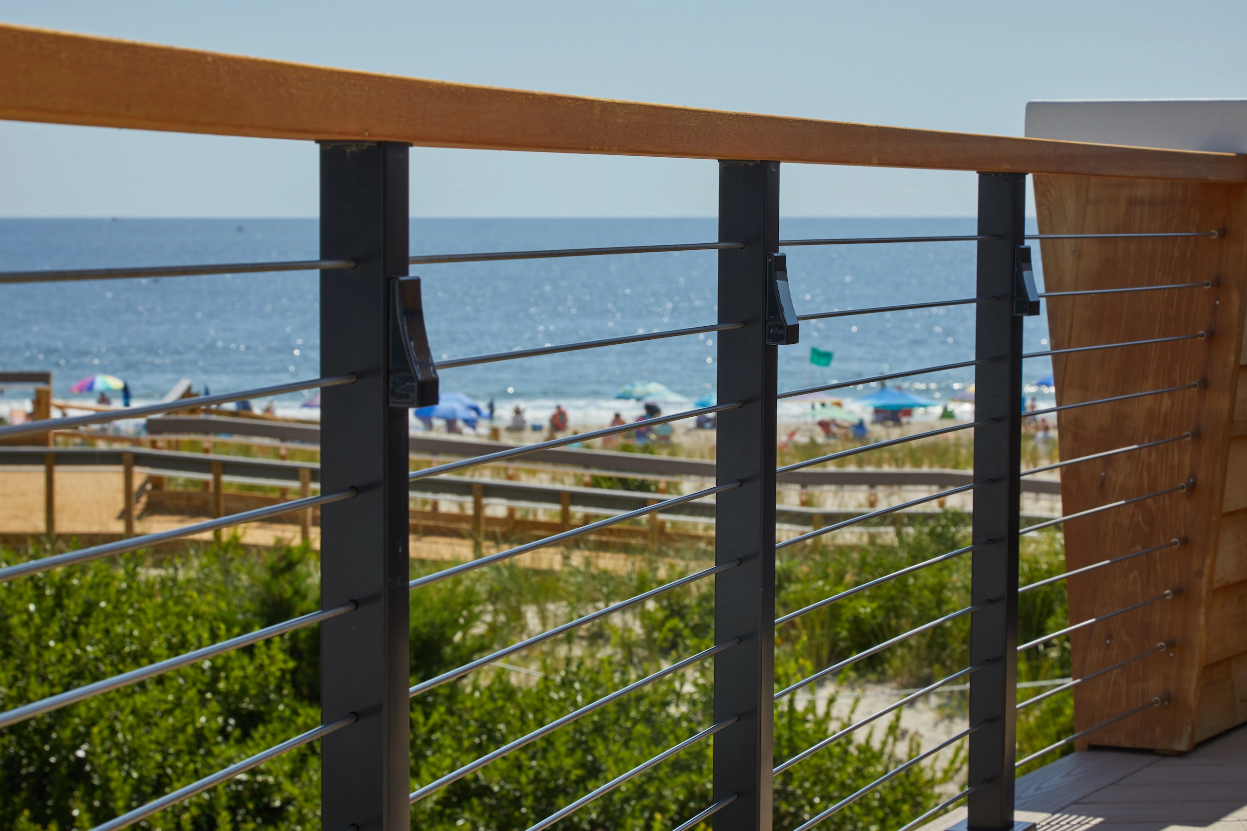 Rod railing with a wood cap opens a deck to an ocean and beach view