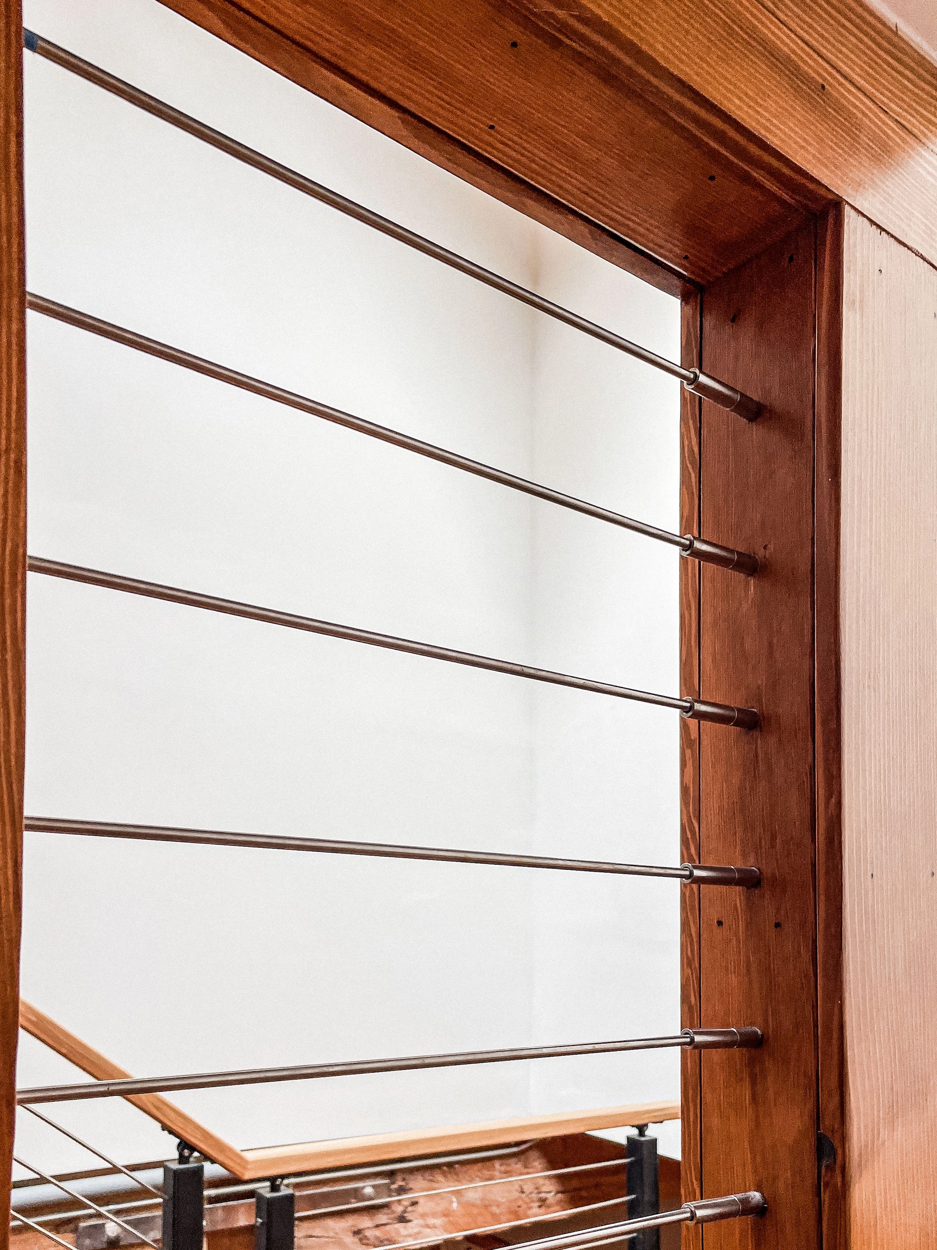 Rods run into a wood post beside an open stairwell in a bright hallway