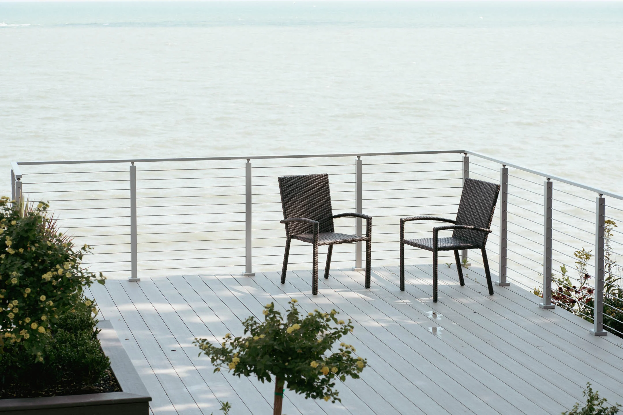Rod railing in white posts encloses a lakeside deck with two patio chairs