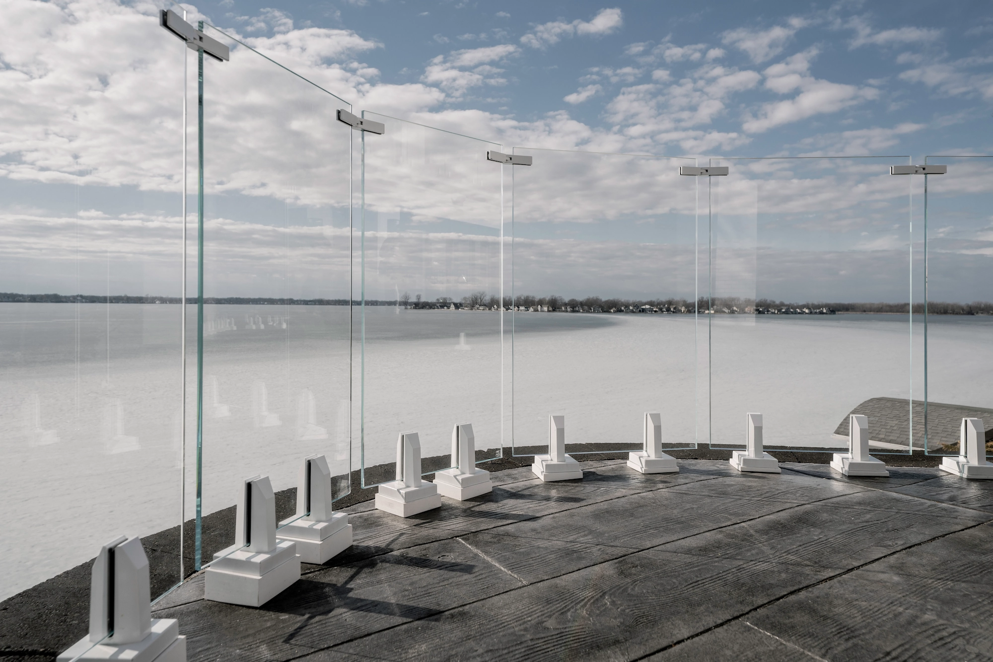 Glass panels on white mounting bases curve around a deck above frozen water