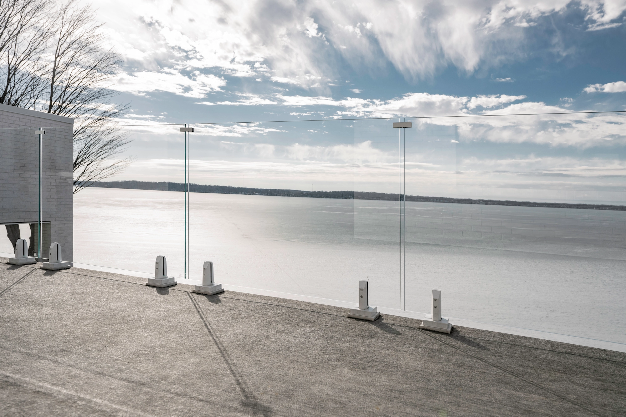 Glass railing spanning a concrete patio with bare trees and open water