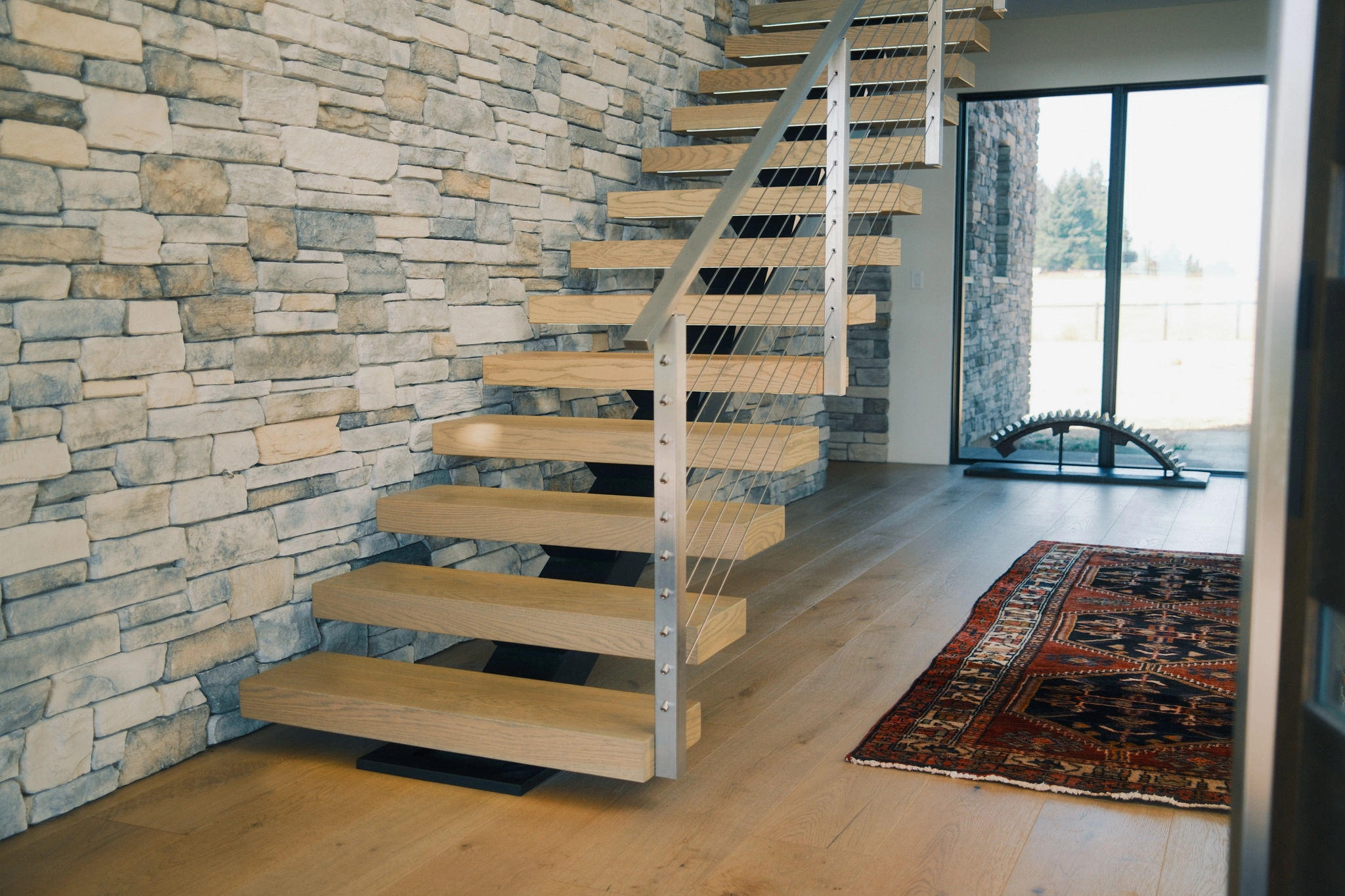 Floating stair rising along a stacked stone wall above wide-plank wood flooring