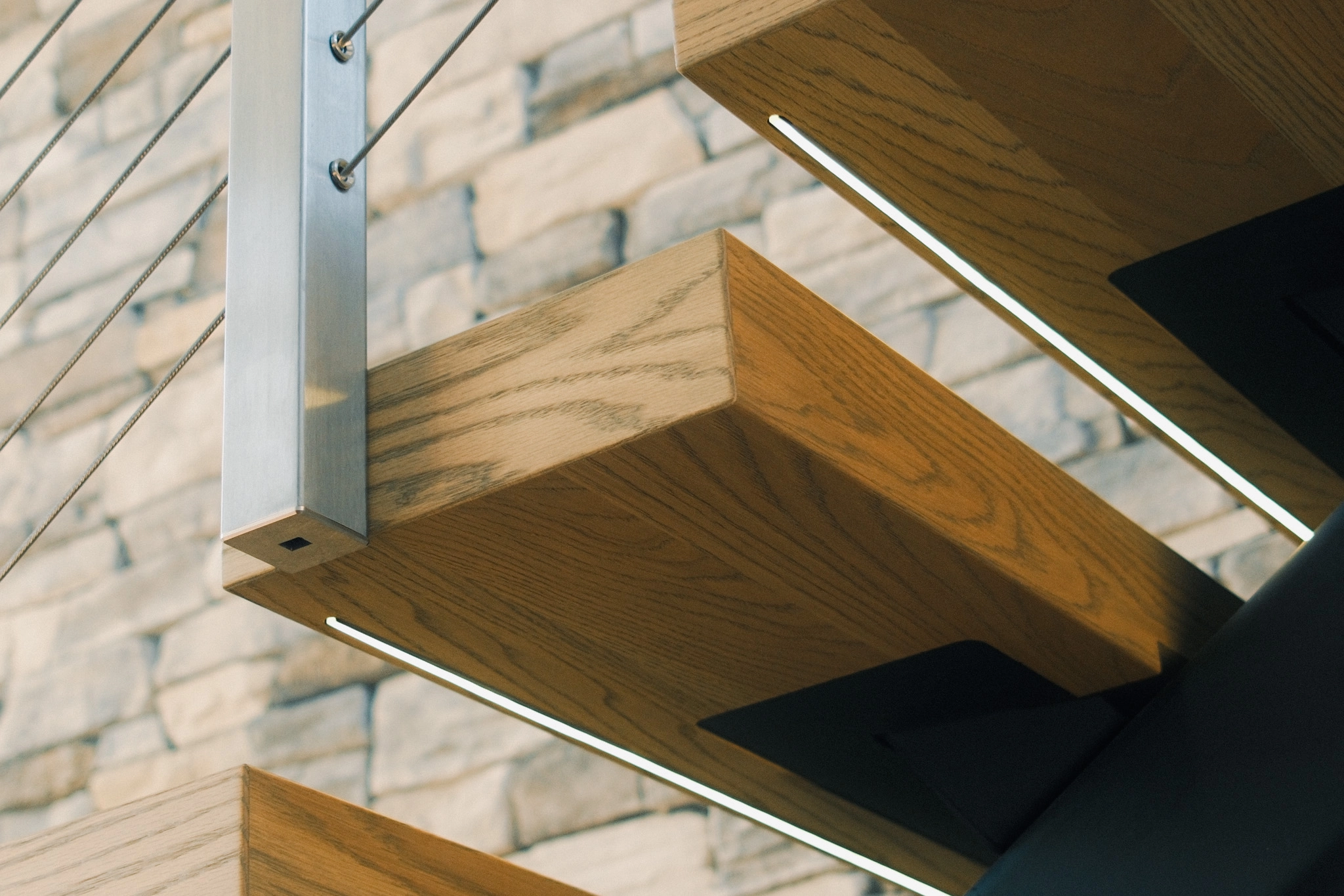 Tread detail with a lit strip along its underside beside a stainless post
