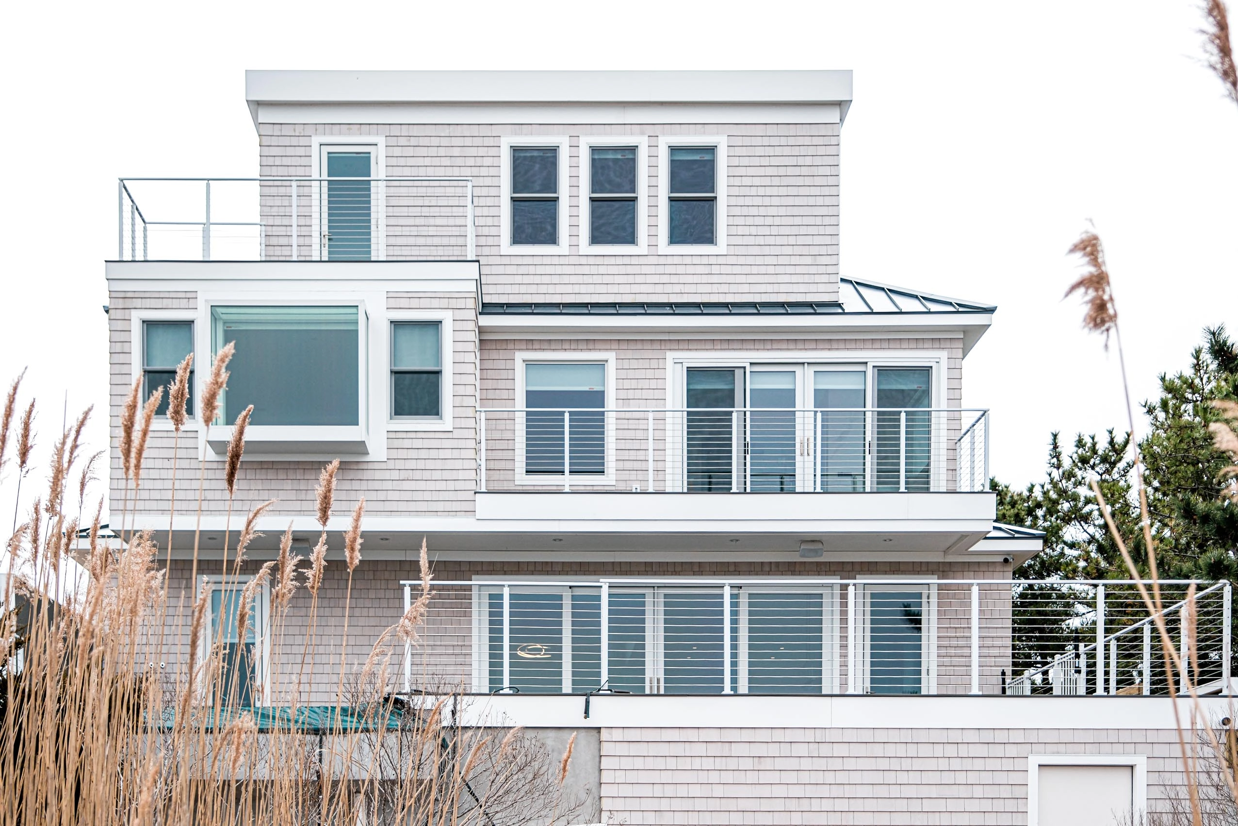 Shingled coastal house with white railing wrapping its upper deck levels