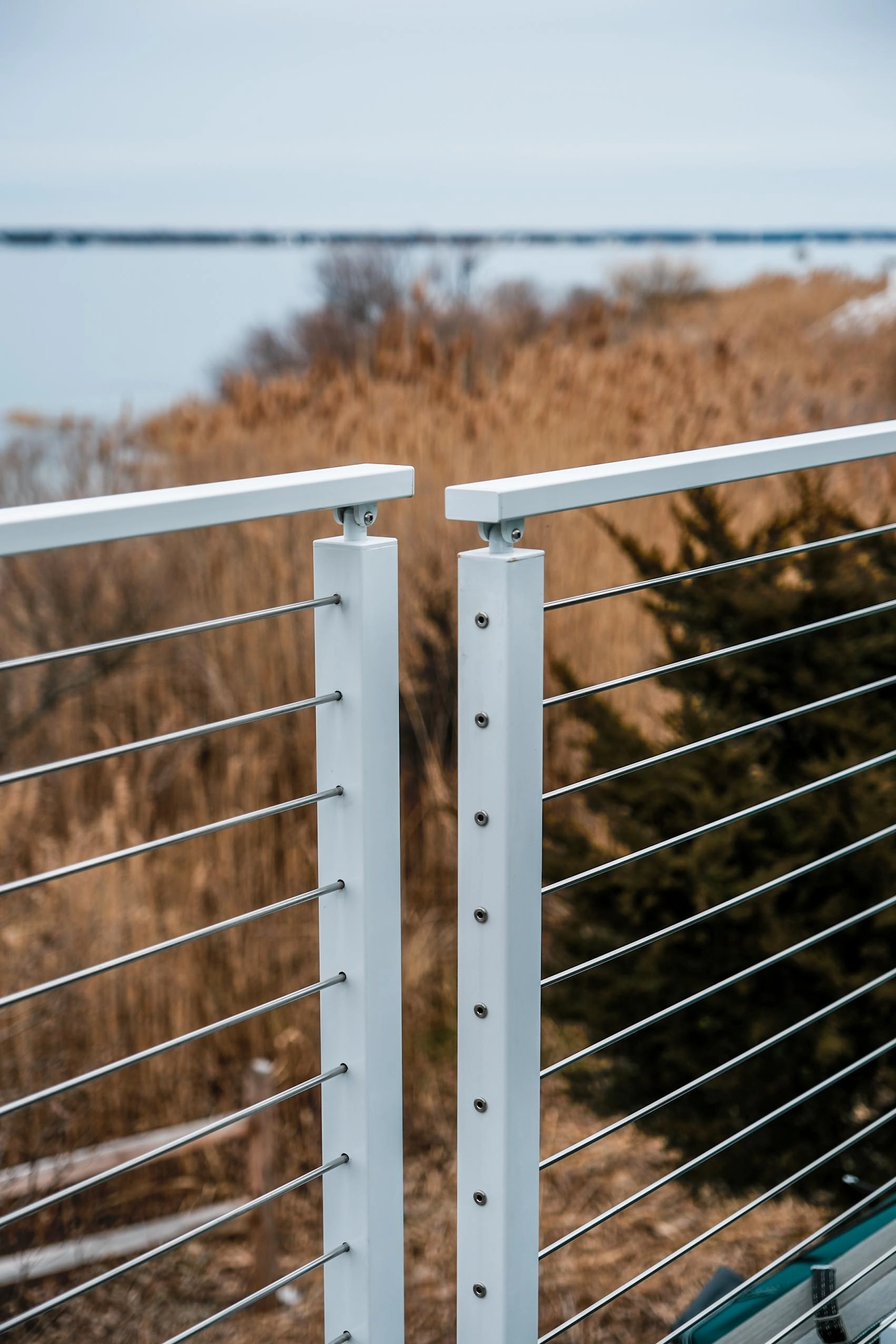 Two white posts meeting where the rod railing turns above marsh grass