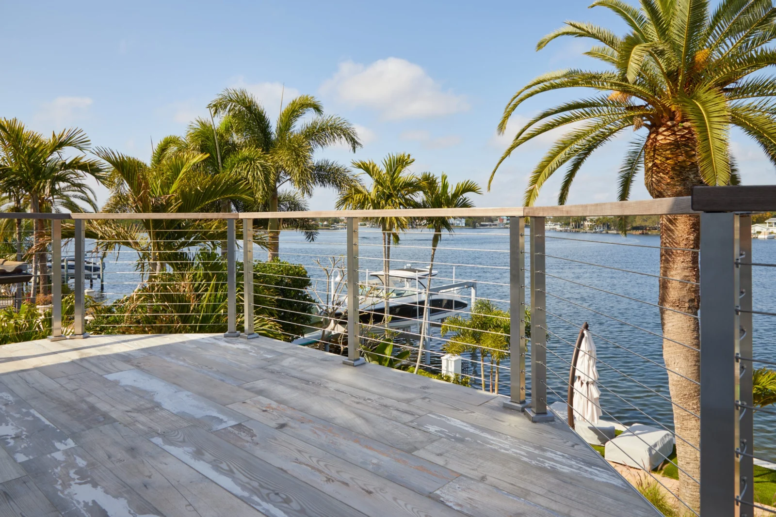Gray plank deck enclosed by cable railing overlooking moored boats and waterway