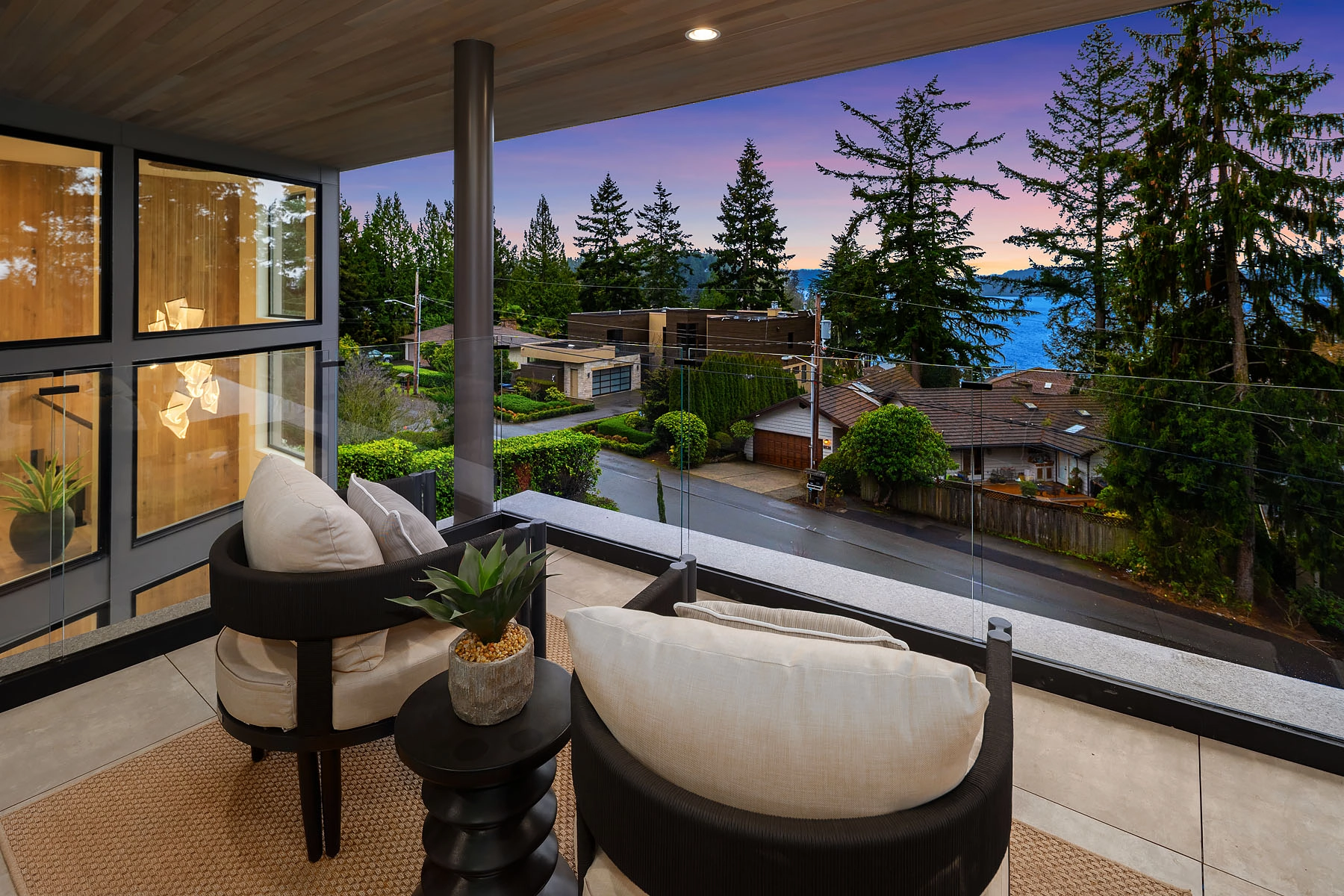 Covered balcony with lounge chairs and glass railing overlooking treetops at sunset