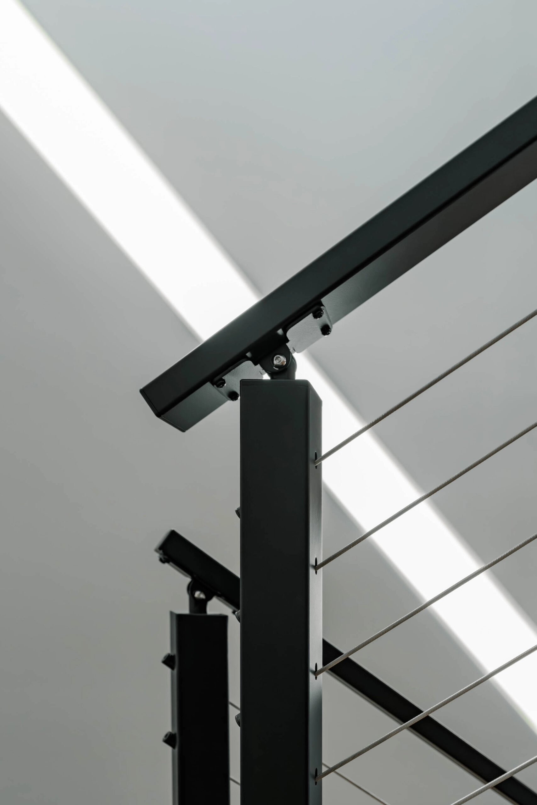 Sunlight across a black top rail and post corner above tight cable runs