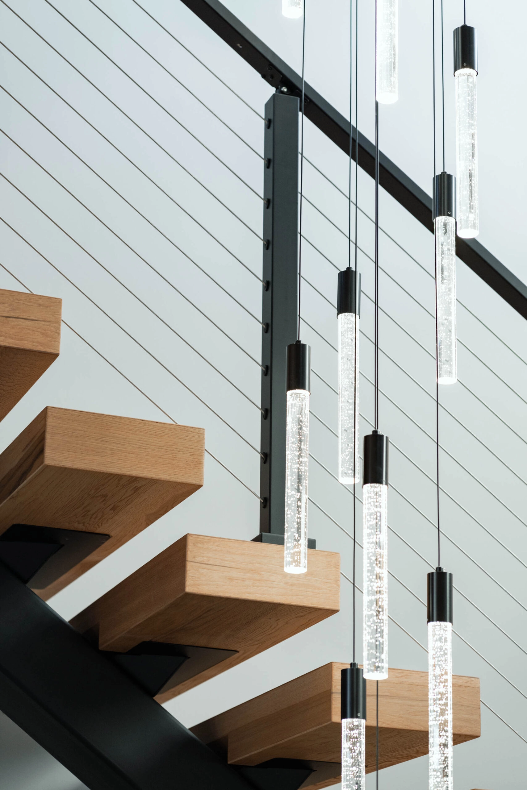 Light wood treads and cable infill against a white shiplap wall with pendants