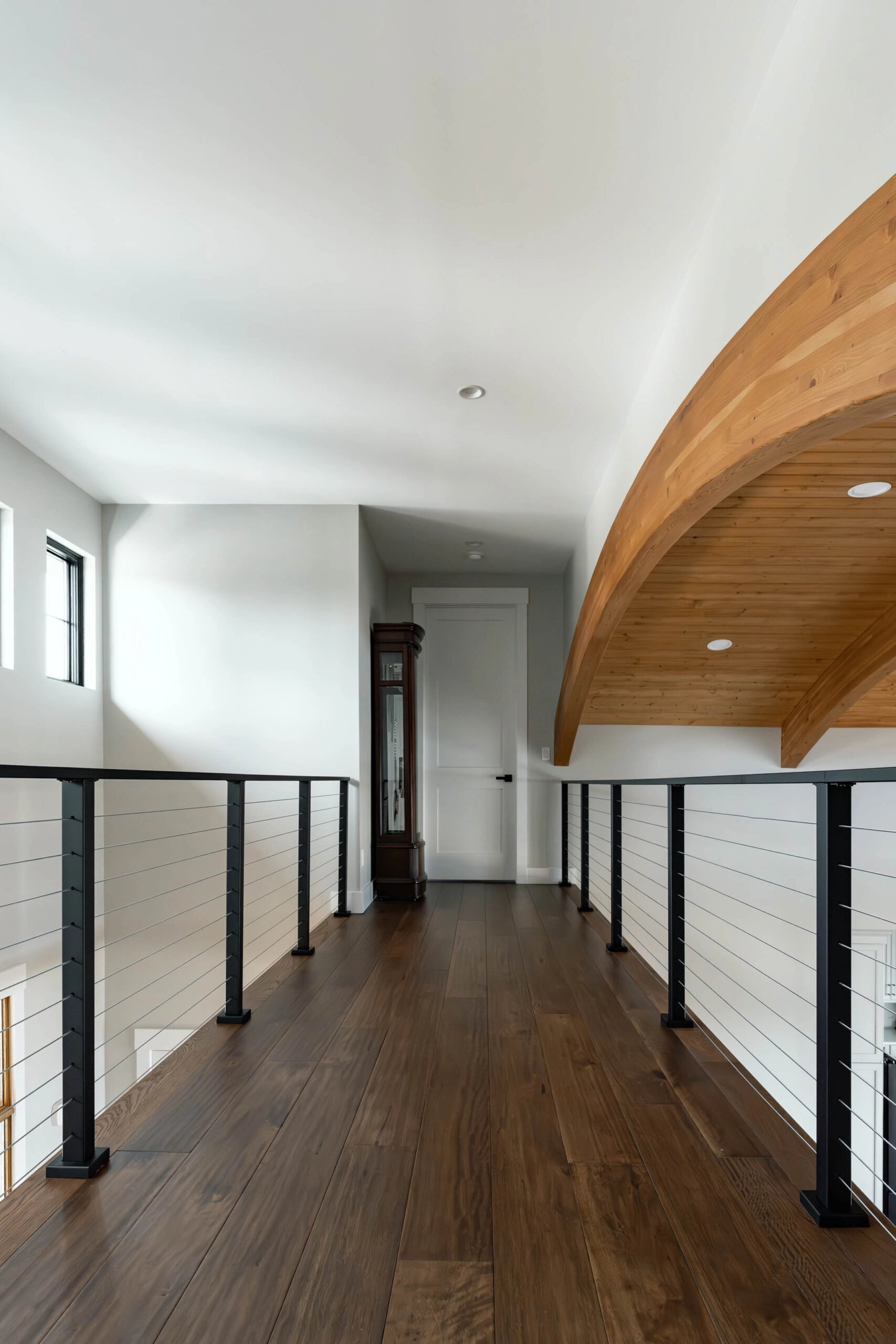 Upper hallway with dark plank floors, cable railing, and a curved wood ceiling
