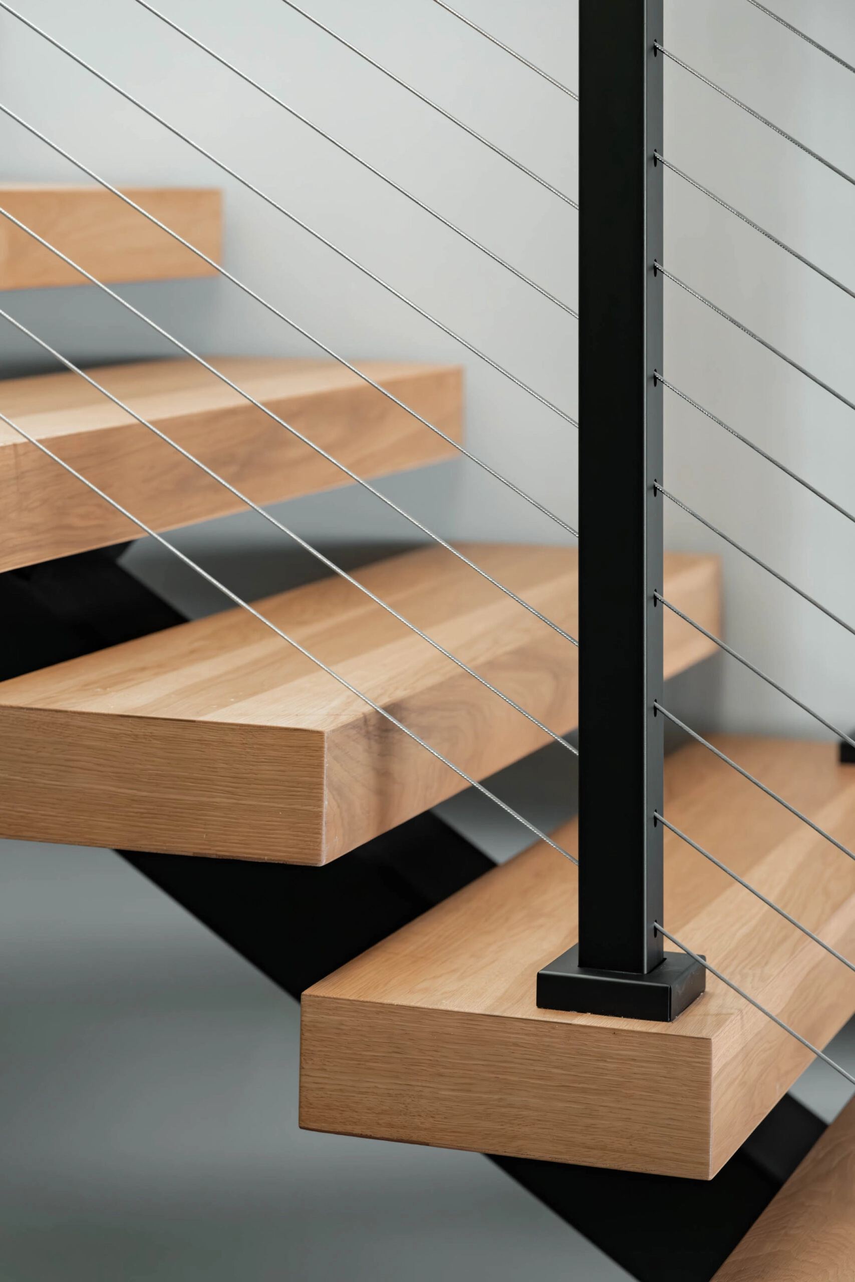 Stacked wood treads with open risers and cables passing behind a black post