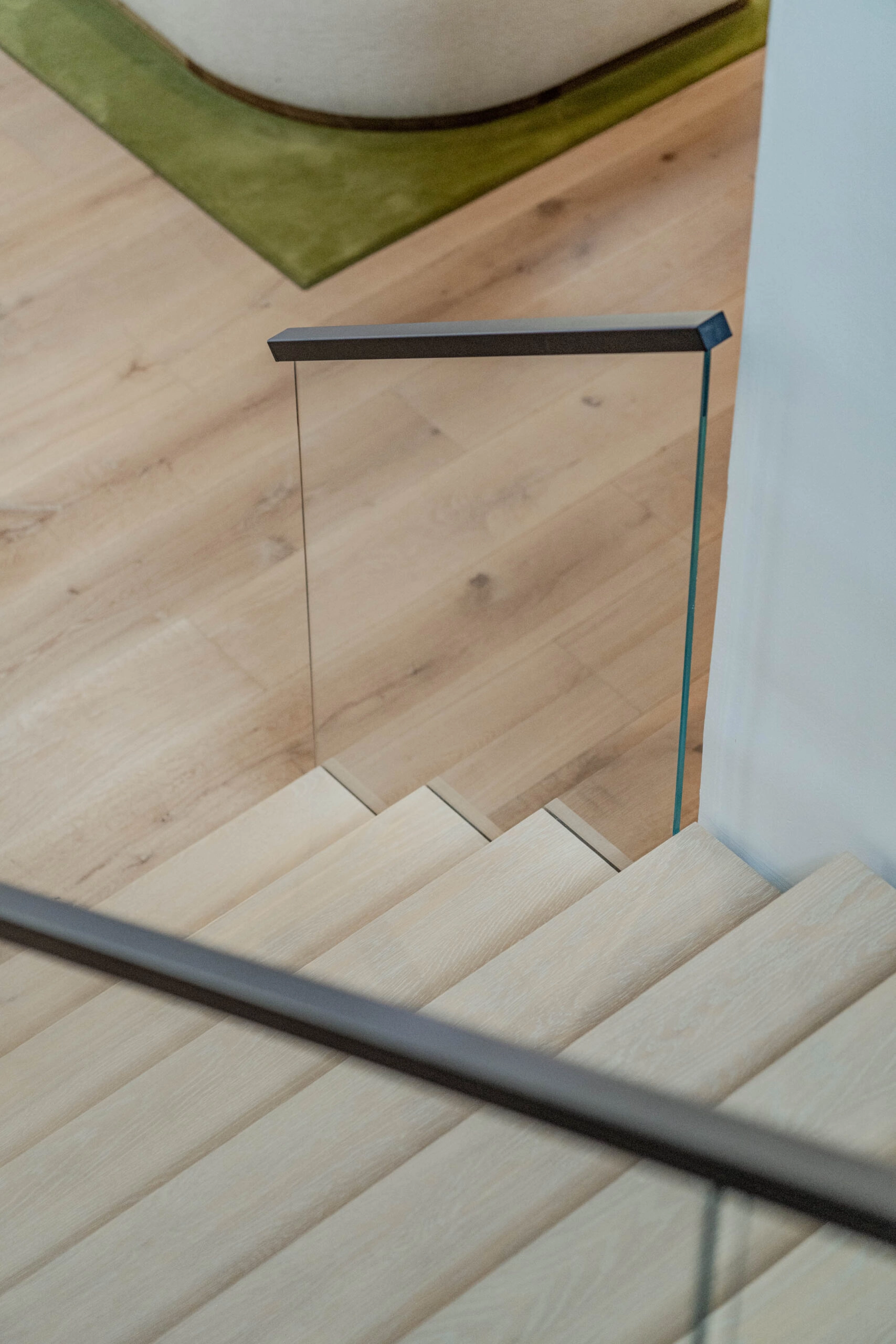 Looking down from the top landing past a glass panel to pale plank flooring