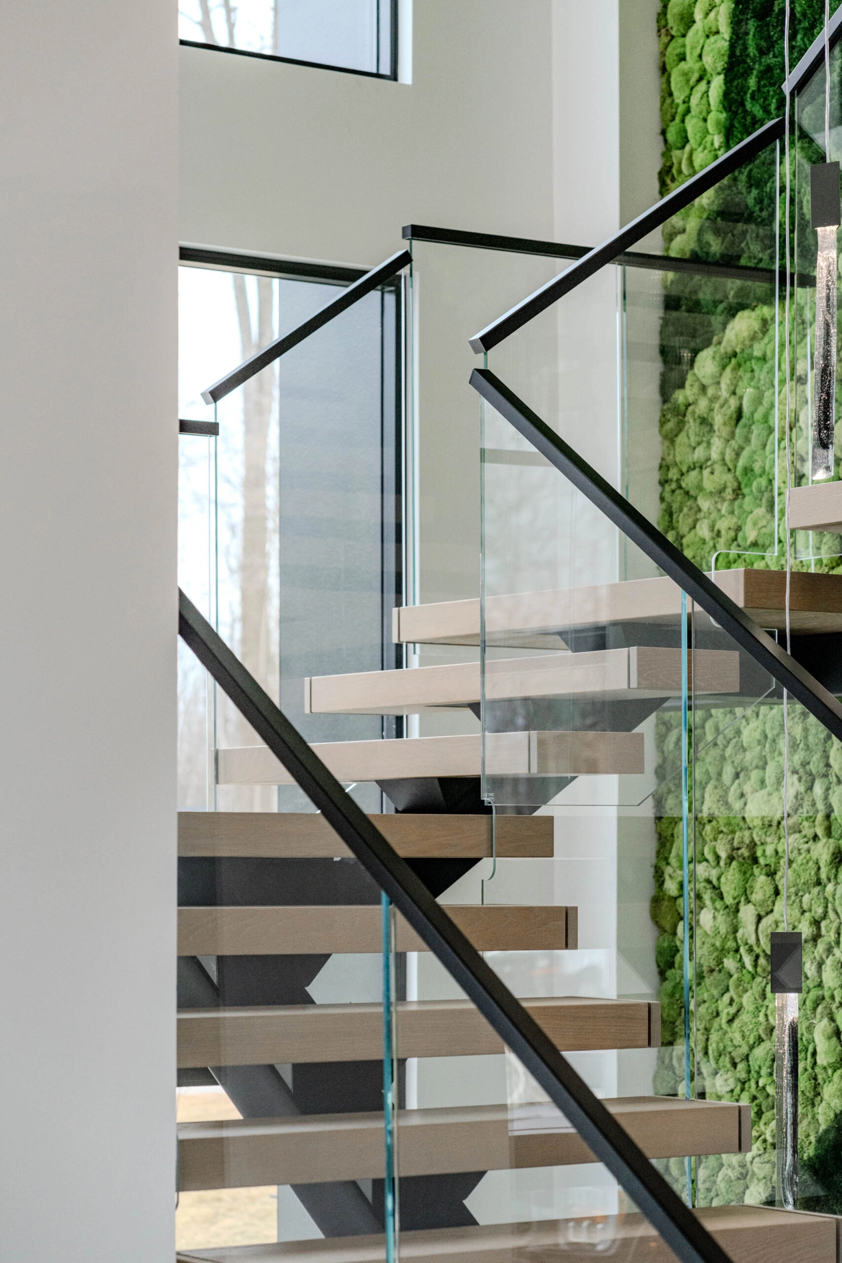 Flight framed by glass panels and a black handrail beside the living wall