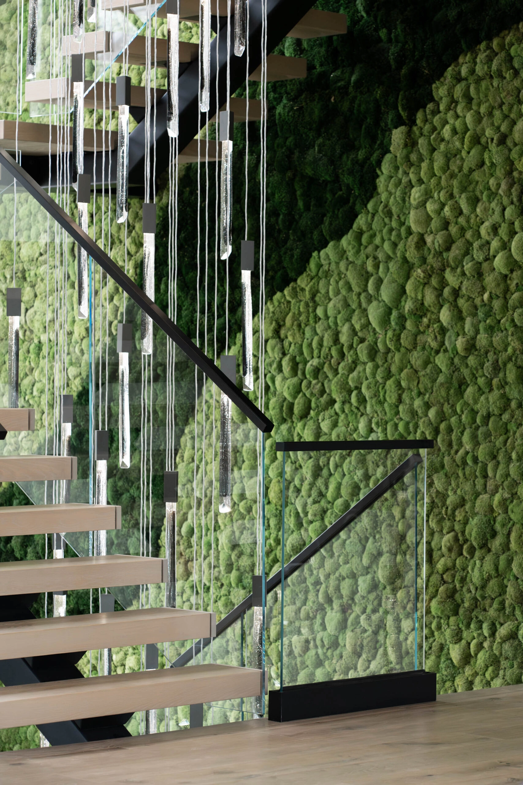 Black base shoe anchoring glass panels where the stair meets the moss wall