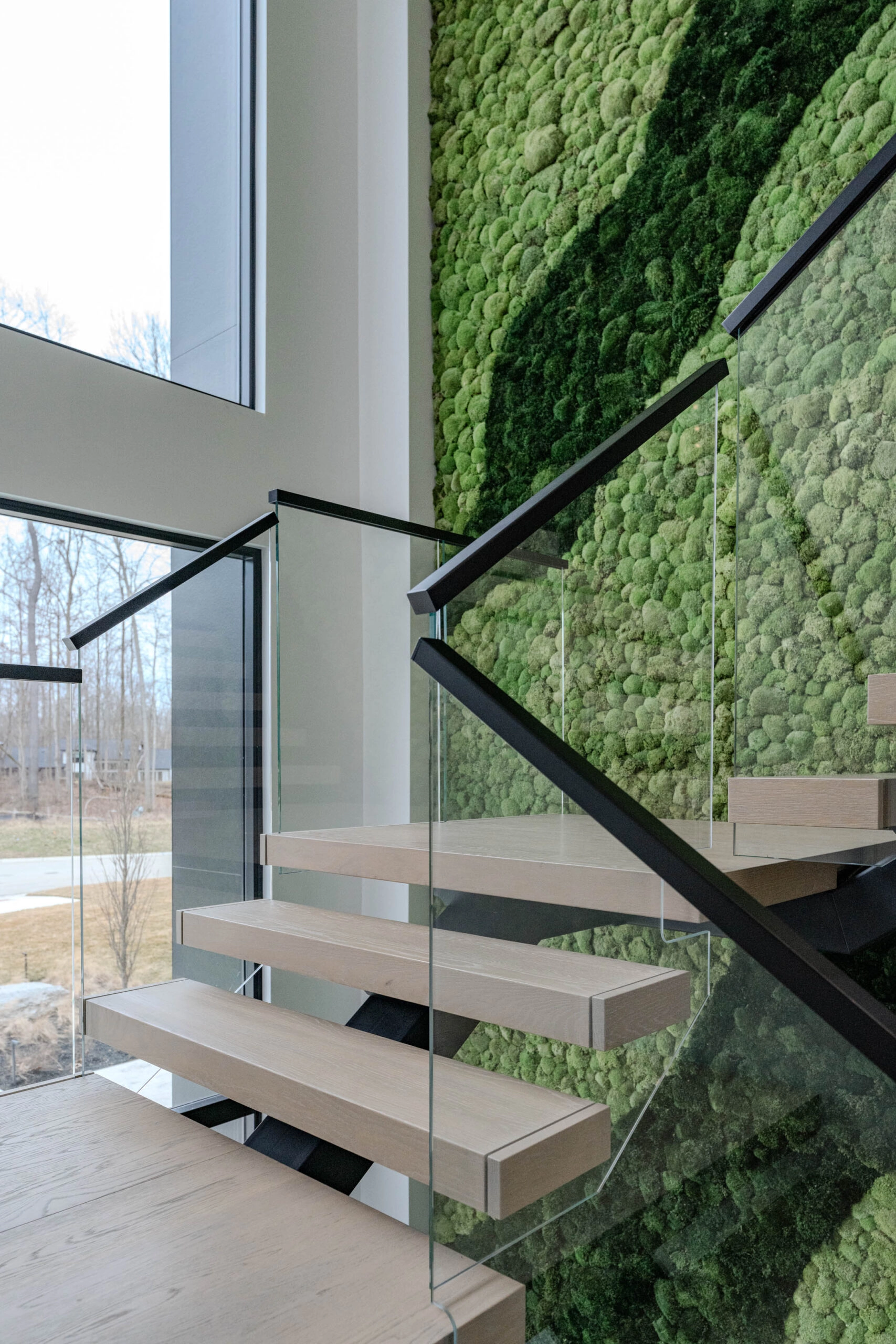 From the bottom landing, glass railing and handrail rise toward a window