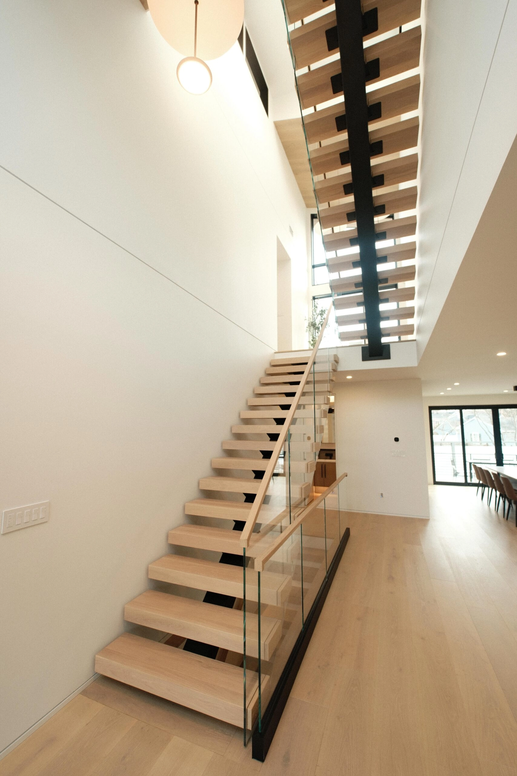 Straight flight rising through a double-height white entry with glass railing