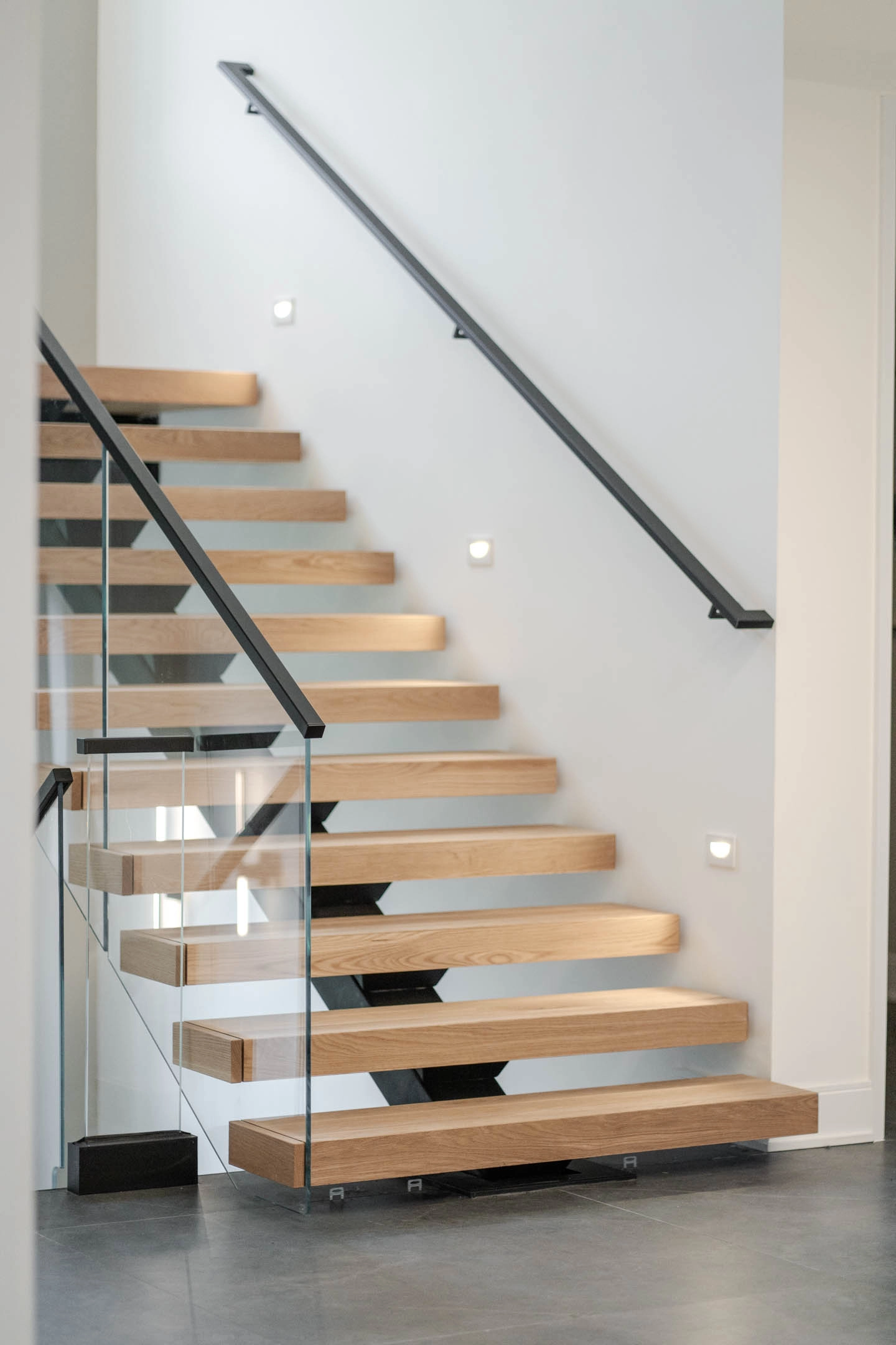 Head-on view of the stair between glass railing and a wall-mounted handrail