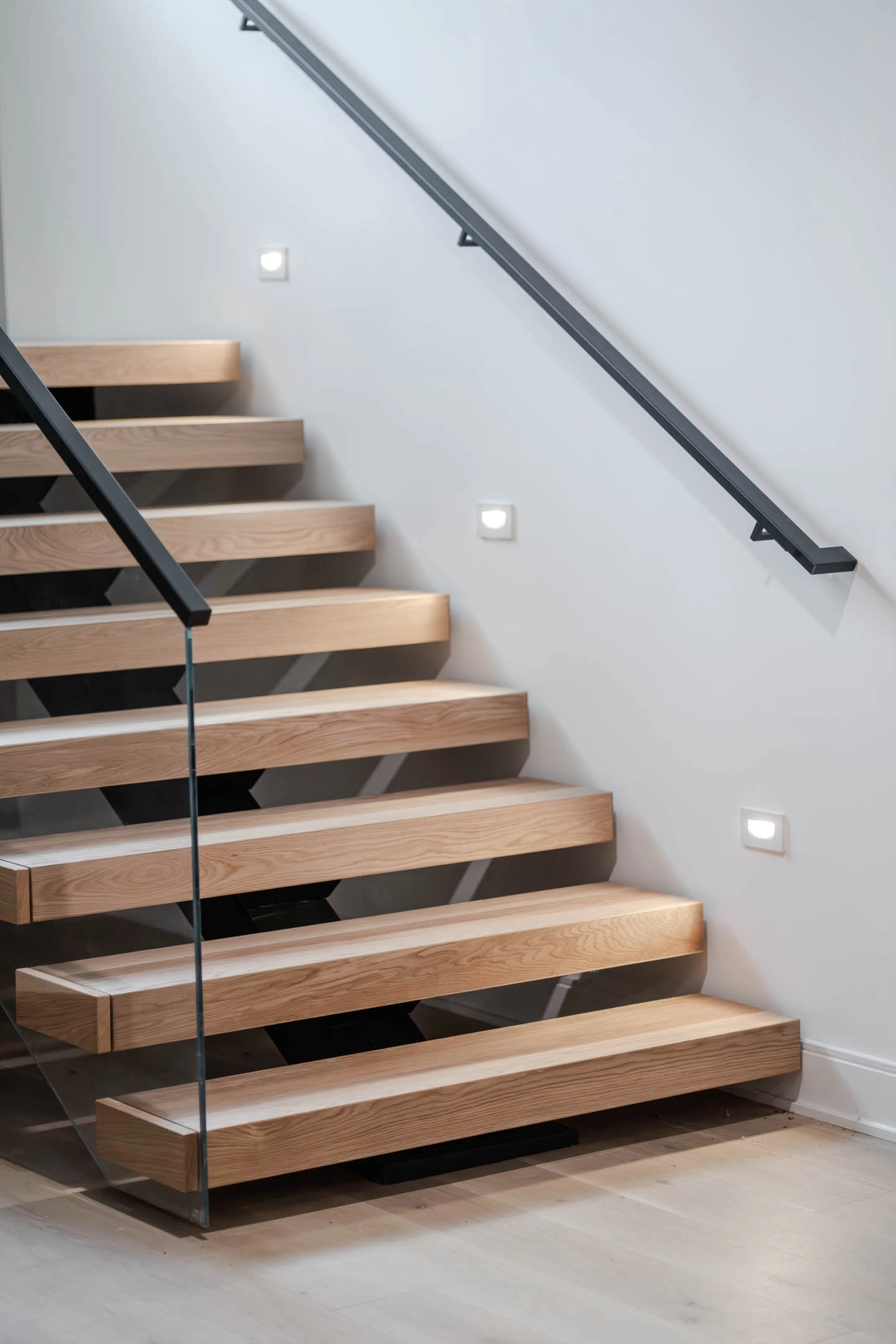 Wall handrail brackets and recessed step lights alongside the floating treads