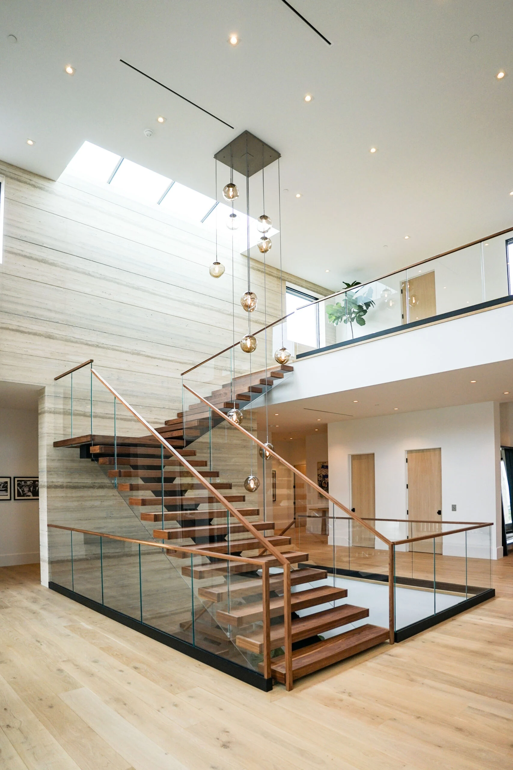 Two-story entry with a wide floating stair, glass railing and pendant cluster