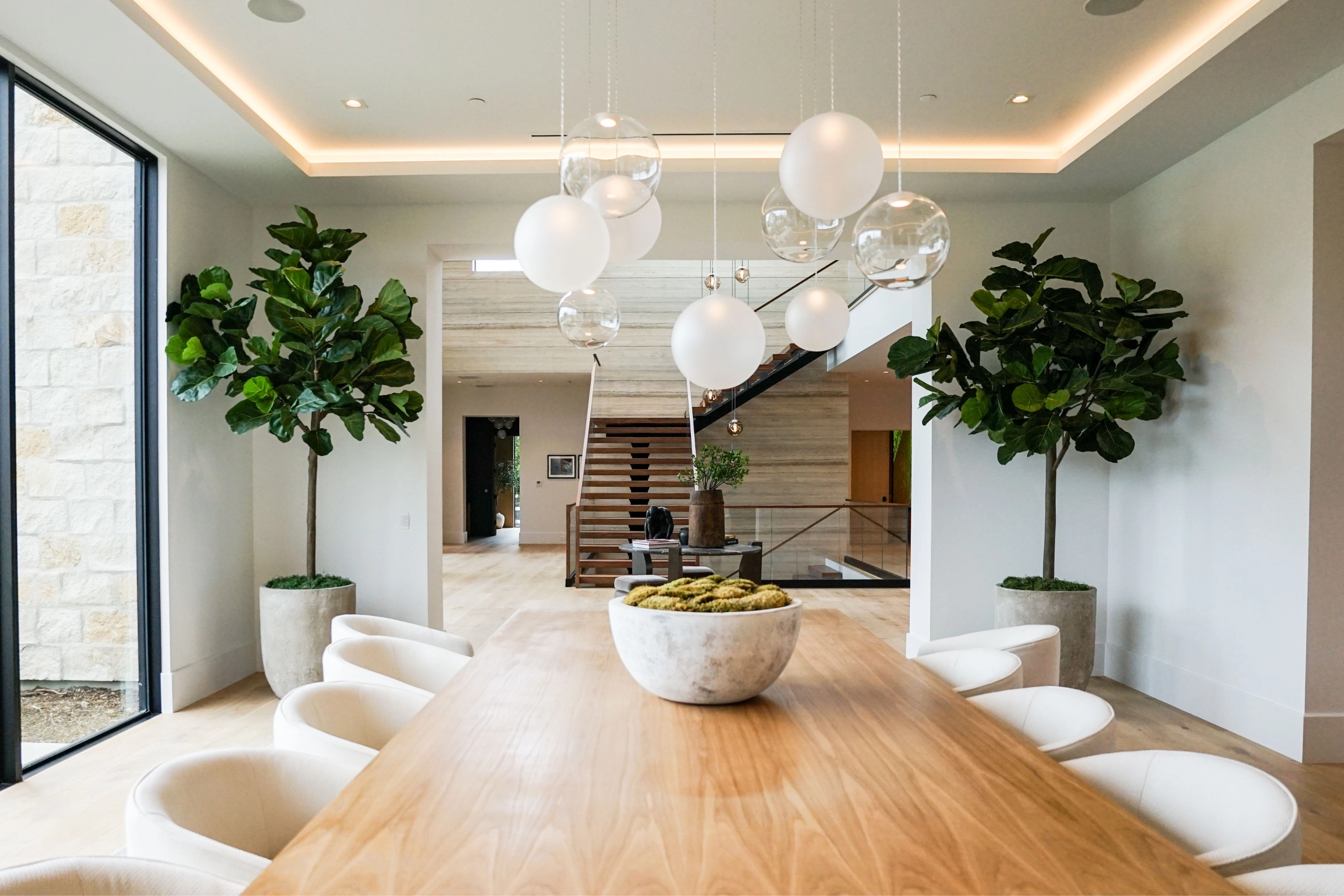 Dining table beneath a cluster of globe pendants with the stair beyond