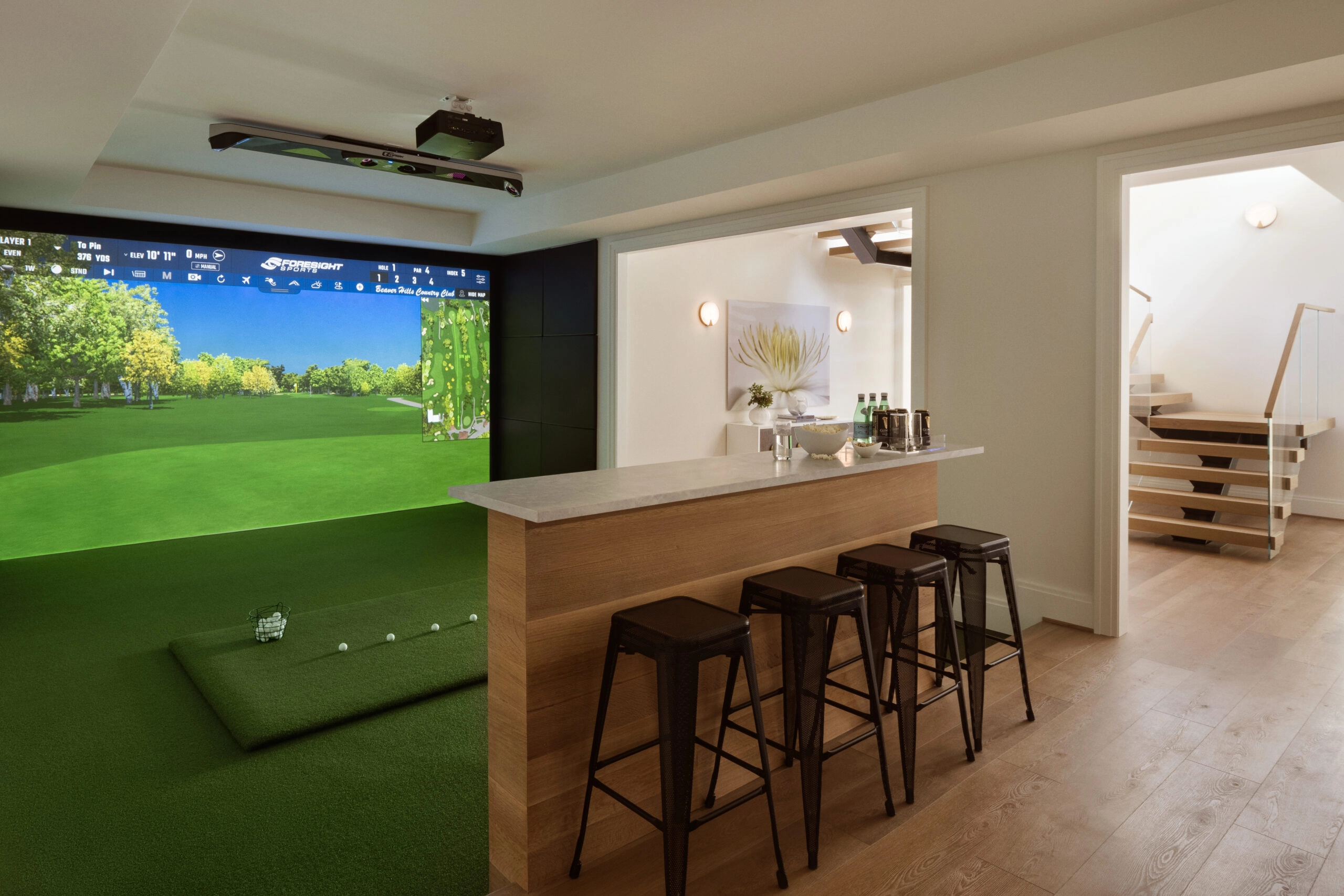 Golf simulator room with a bar counter, stools and the stair landing beyond