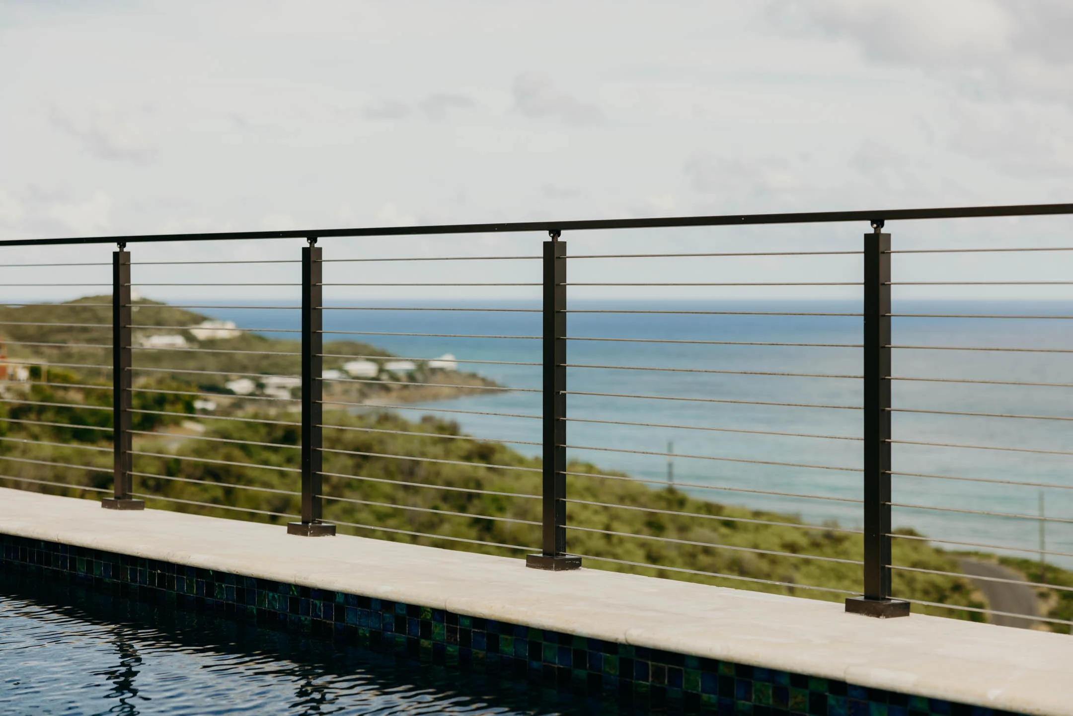 Evenly spaced rods between square black posts beside a tiled pool edge
