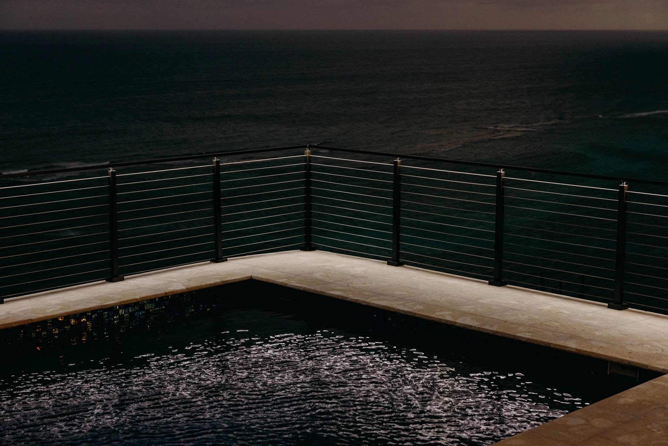 Rod railing framing a dark pool corner at dusk above the water