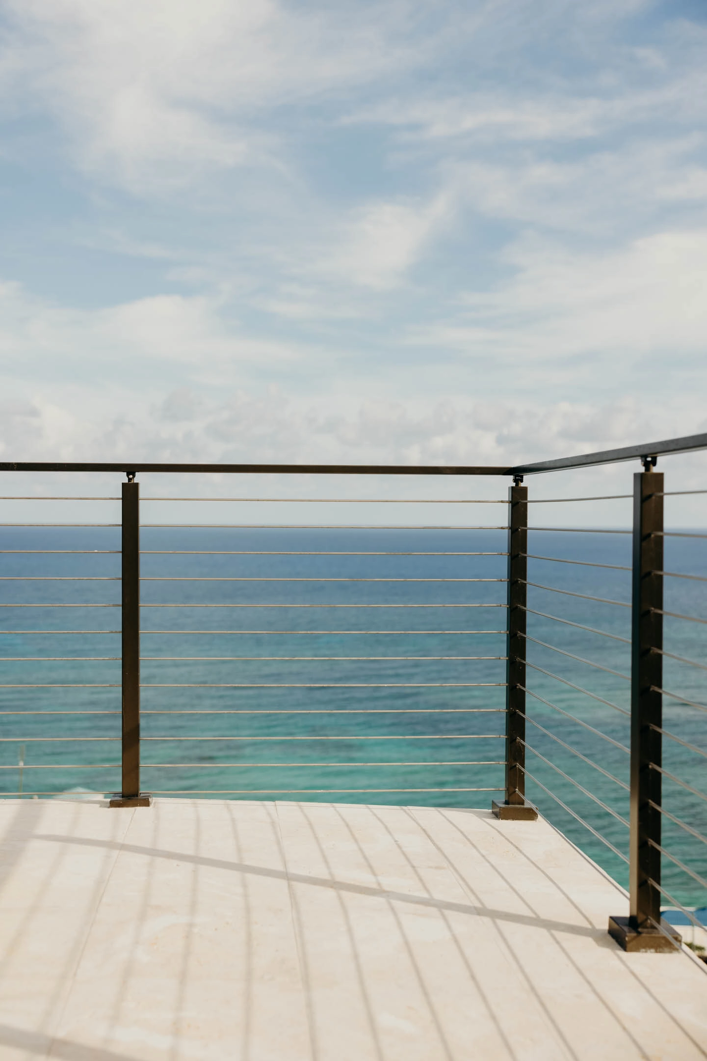 Rod railing corner on a pale stone deck facing calm blue water