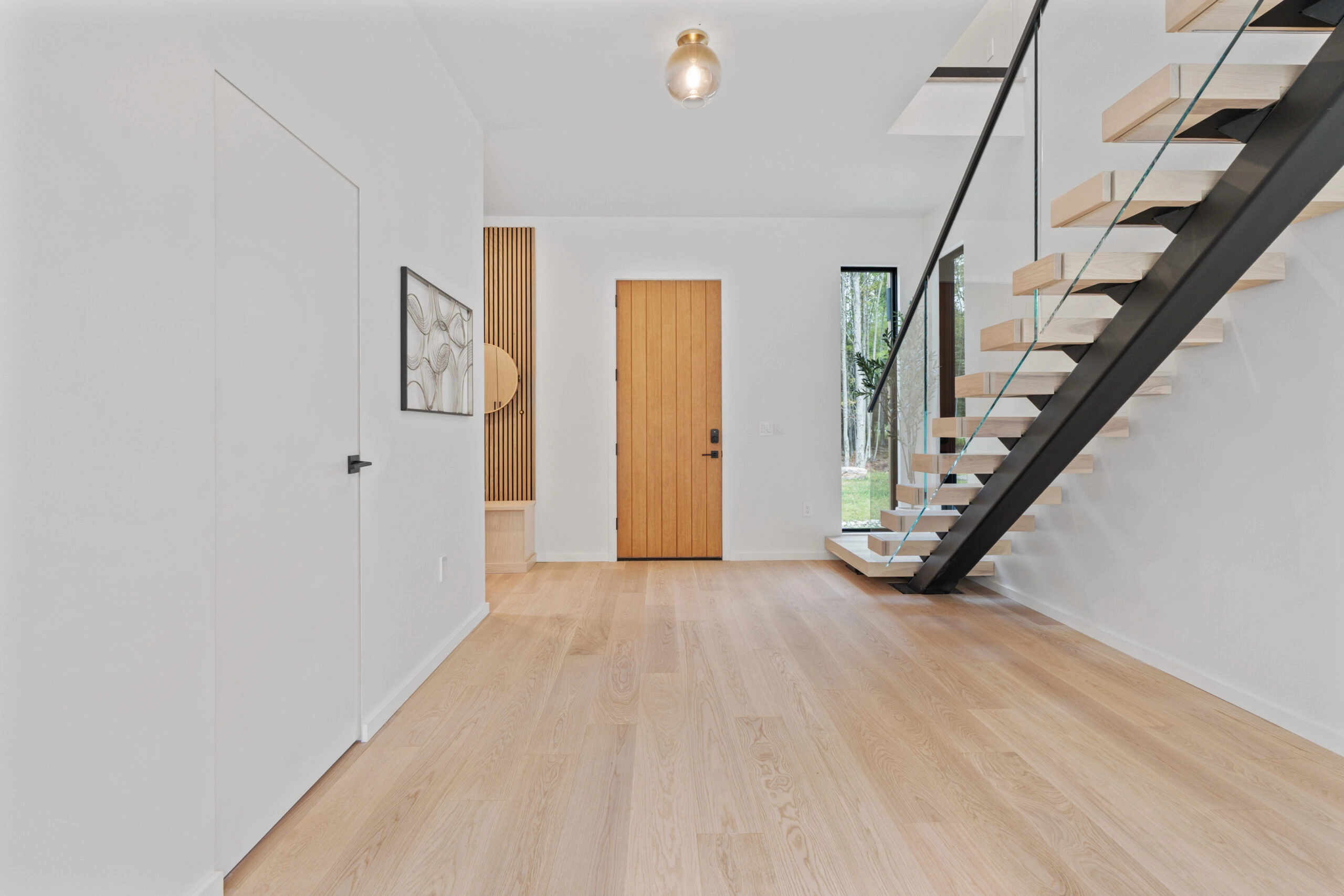 Entry hall with plank floor and a floating stair on a black stringer