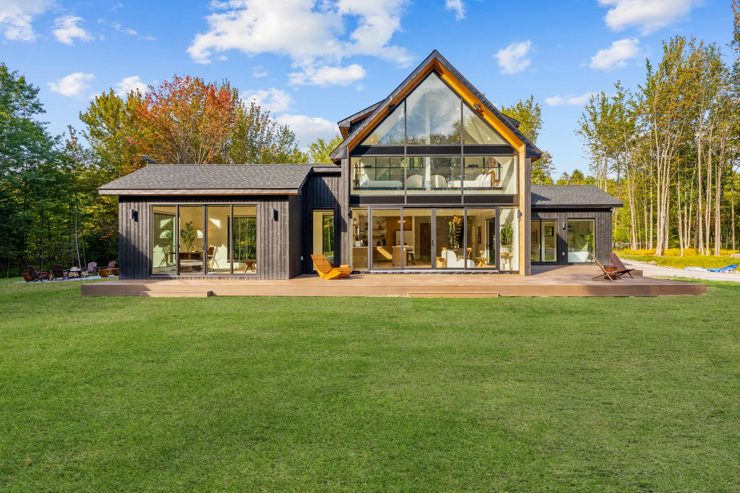 Dark-clad gabled house with tall glass gable seen across a mown lawn