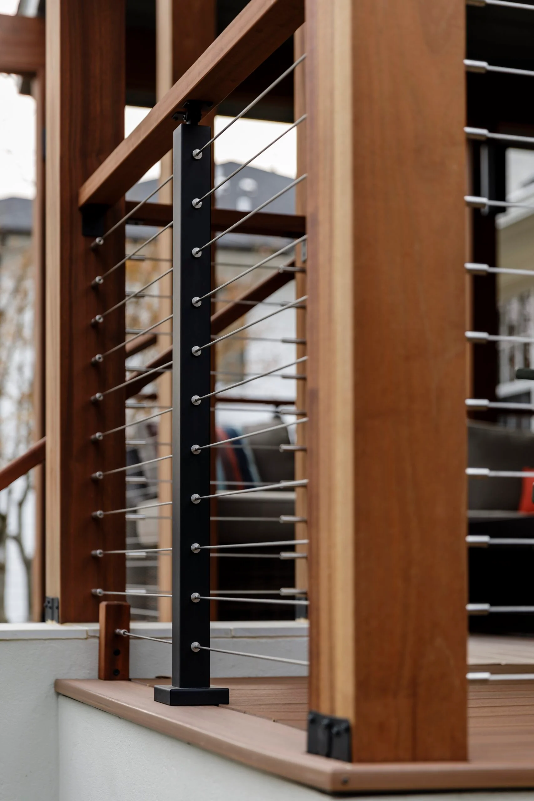 Black post carrying taut cables between wood top rails on a porch