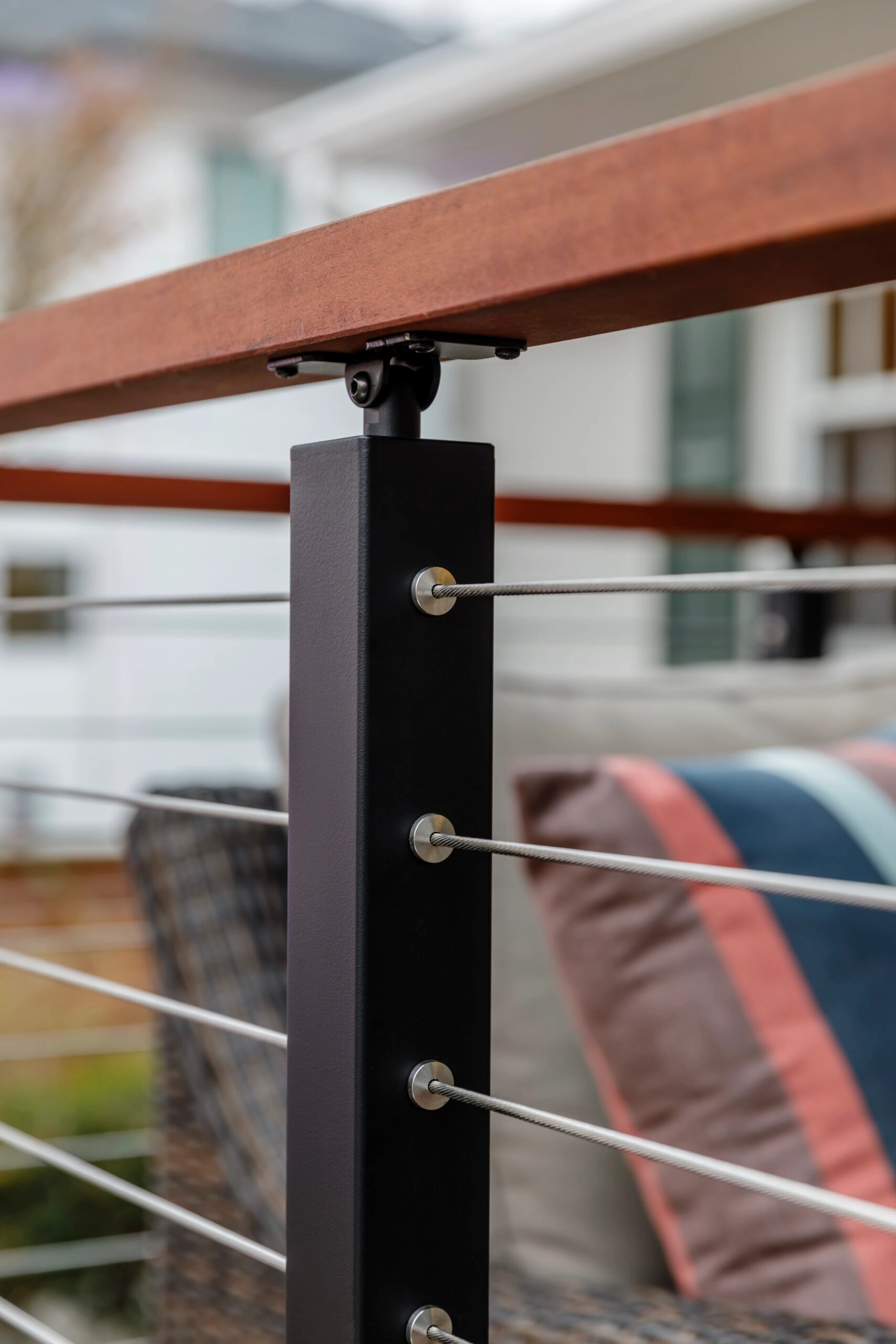 Black post head under a wood top rail with cables and cushions behind