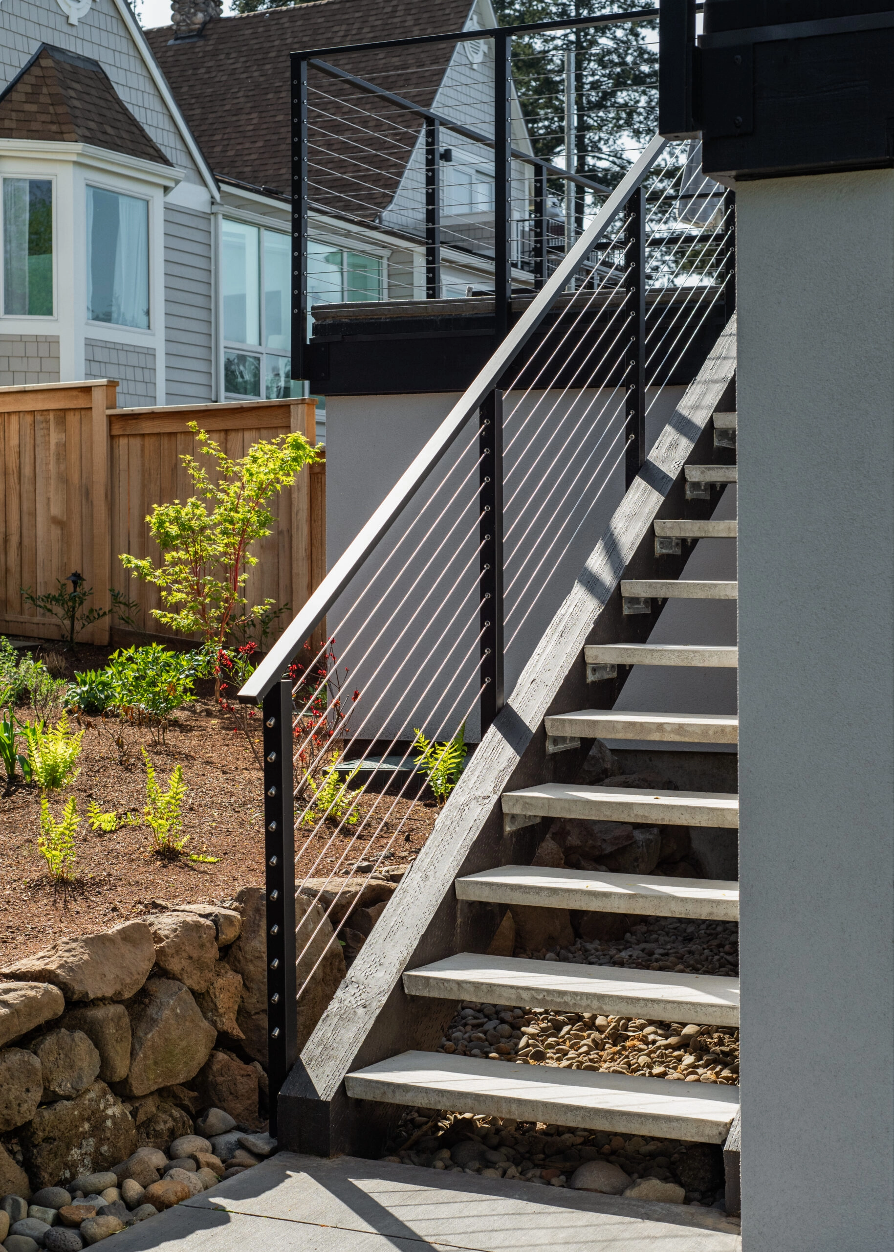 Side-mounted Signature Cable Railing with black posts and black metal handrail climbs an open-riser wooden staircase to an outdoor detached deck. 