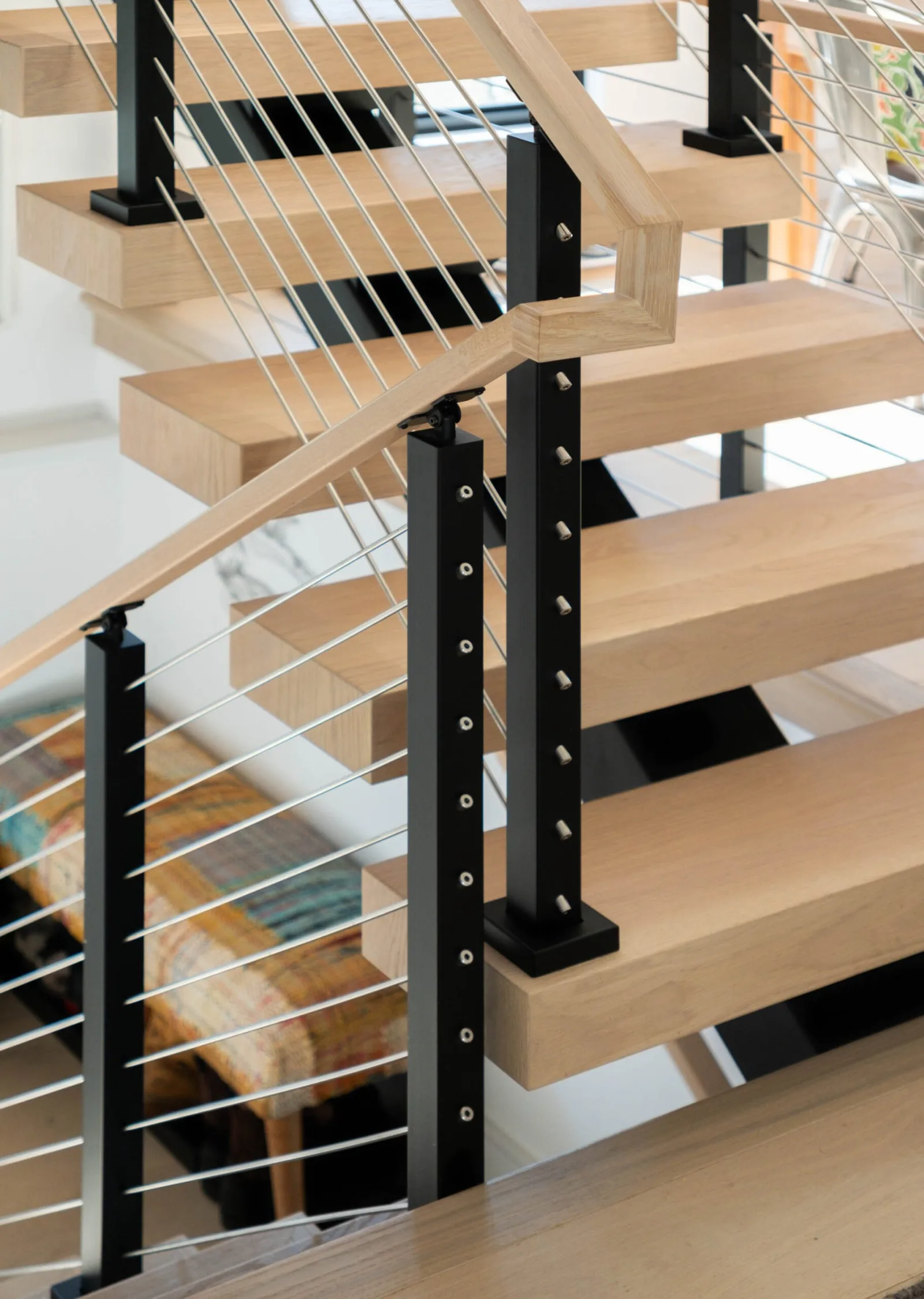 Black post and stainless rod infill at the turn below a wood top rail
