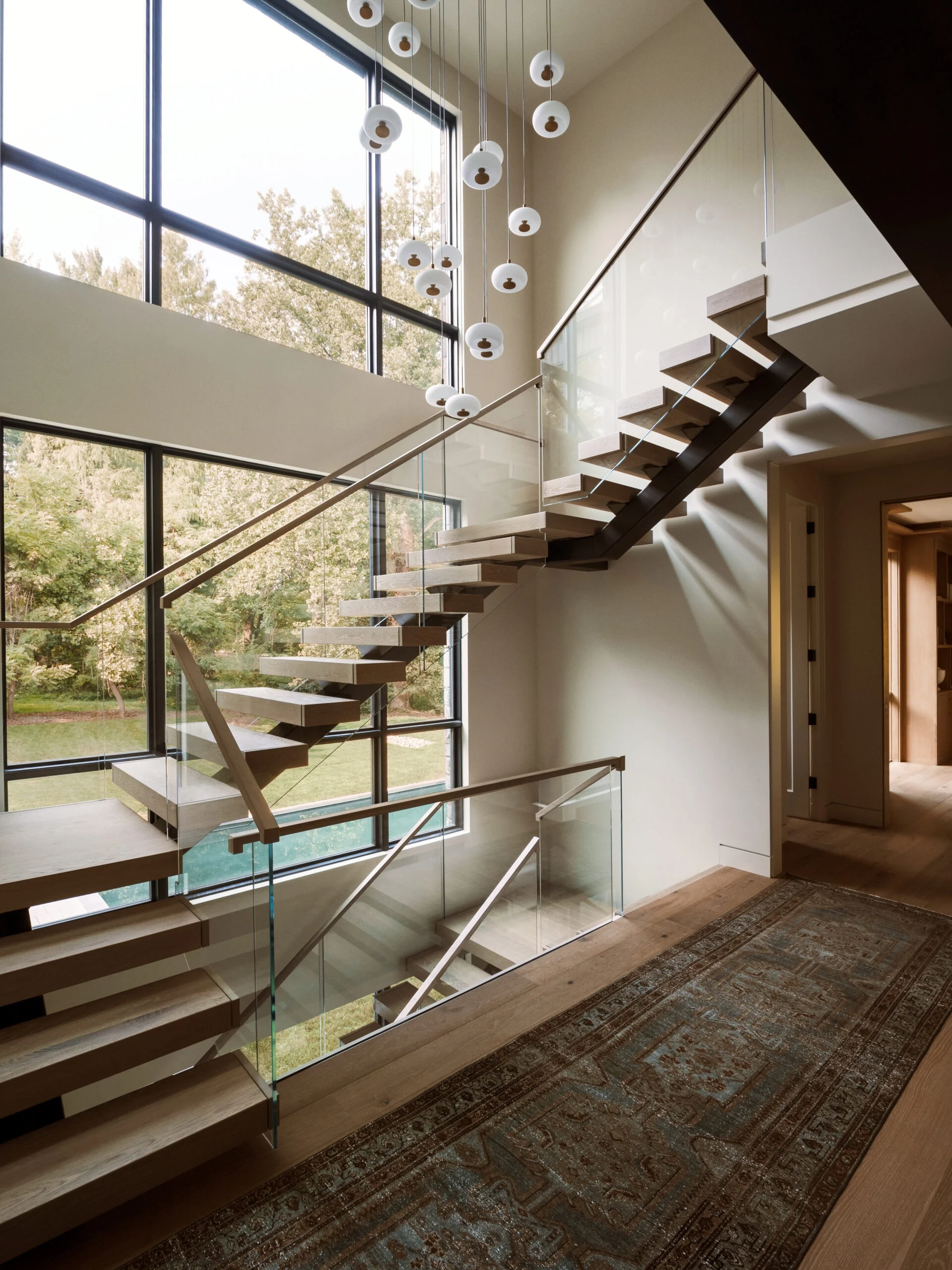 Floating stair with glass railing against black-framed windows and pendant globes