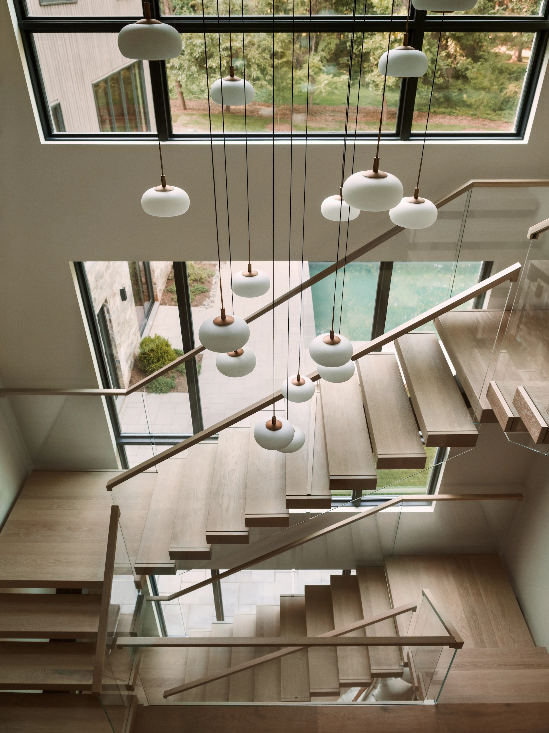 Looking down at the treads, glass railing and hanging globe lights