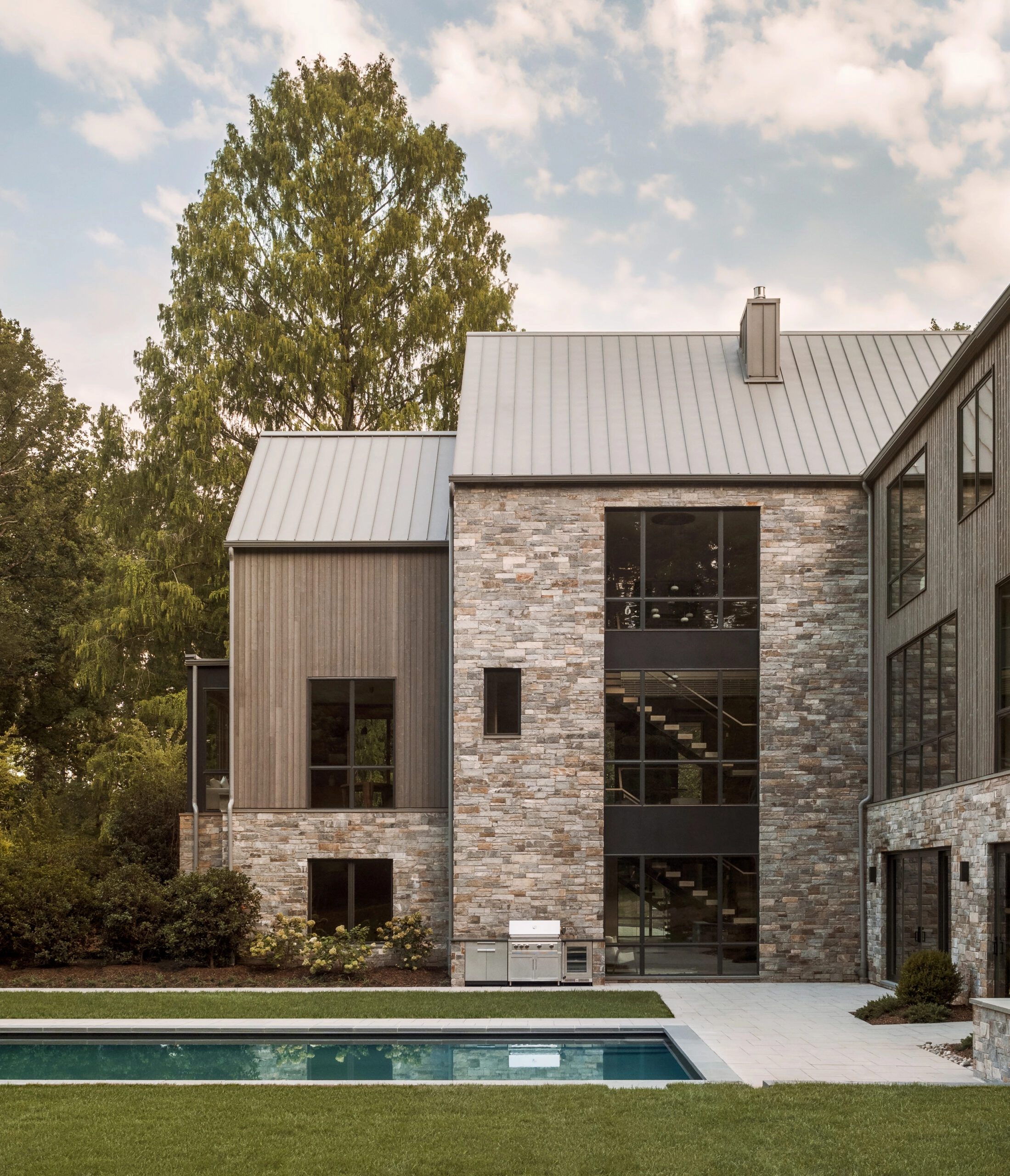 Stone and wood-clad house with the stair visible through two-story glazing