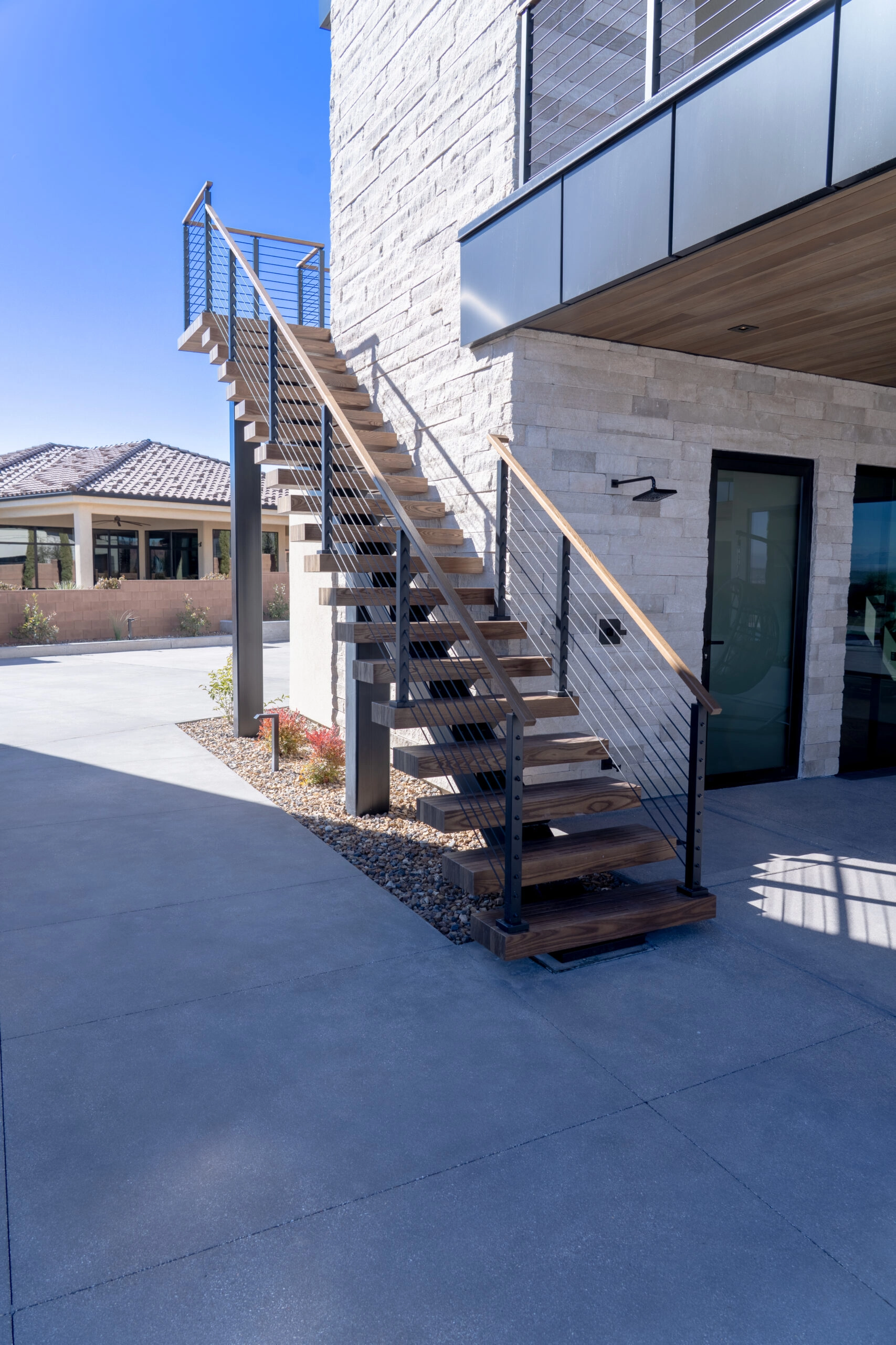 Outdoor stair with cable railing descending along a stone-clad wall