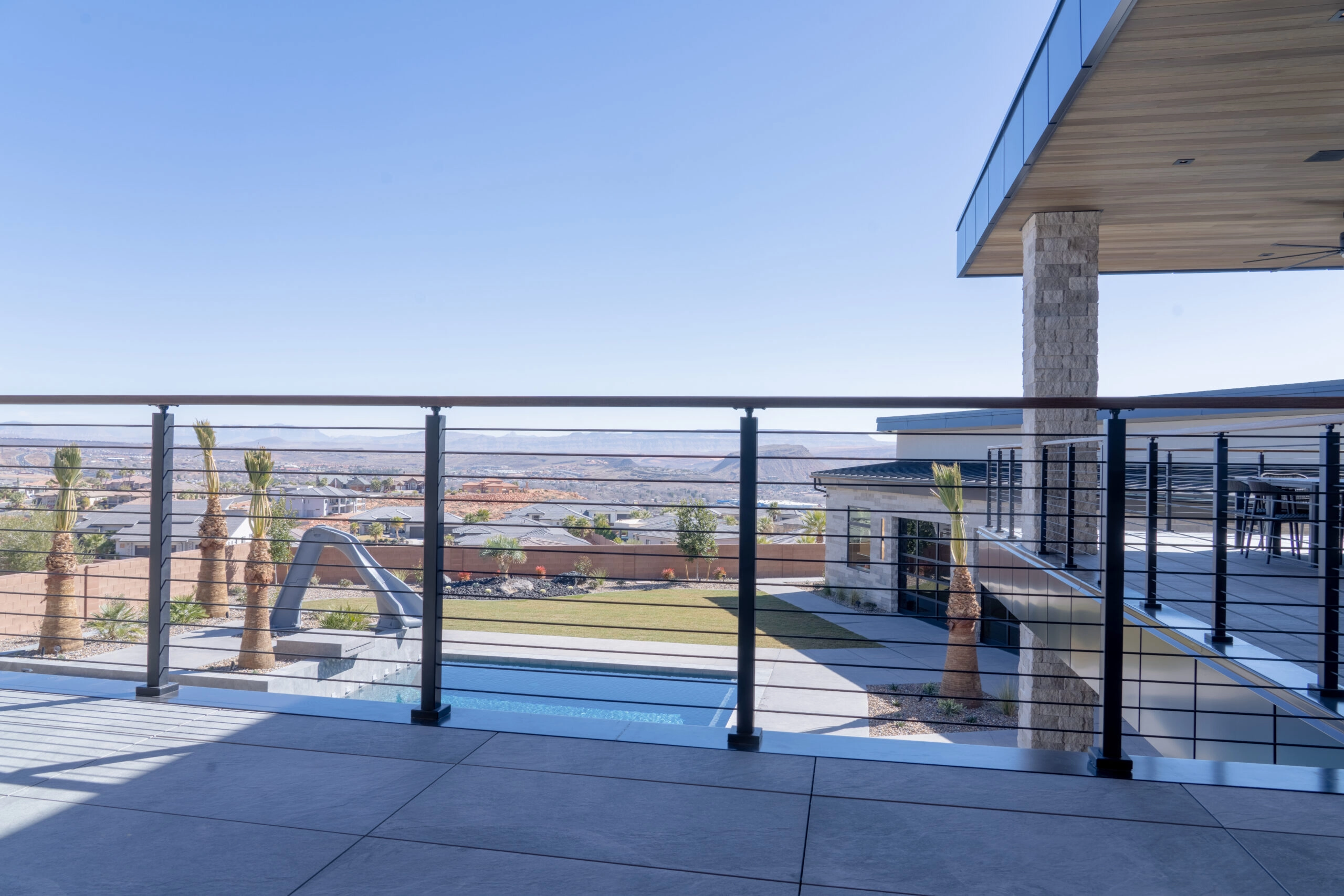 Cable railing along a terrace overlooking palms, a pool and open valley