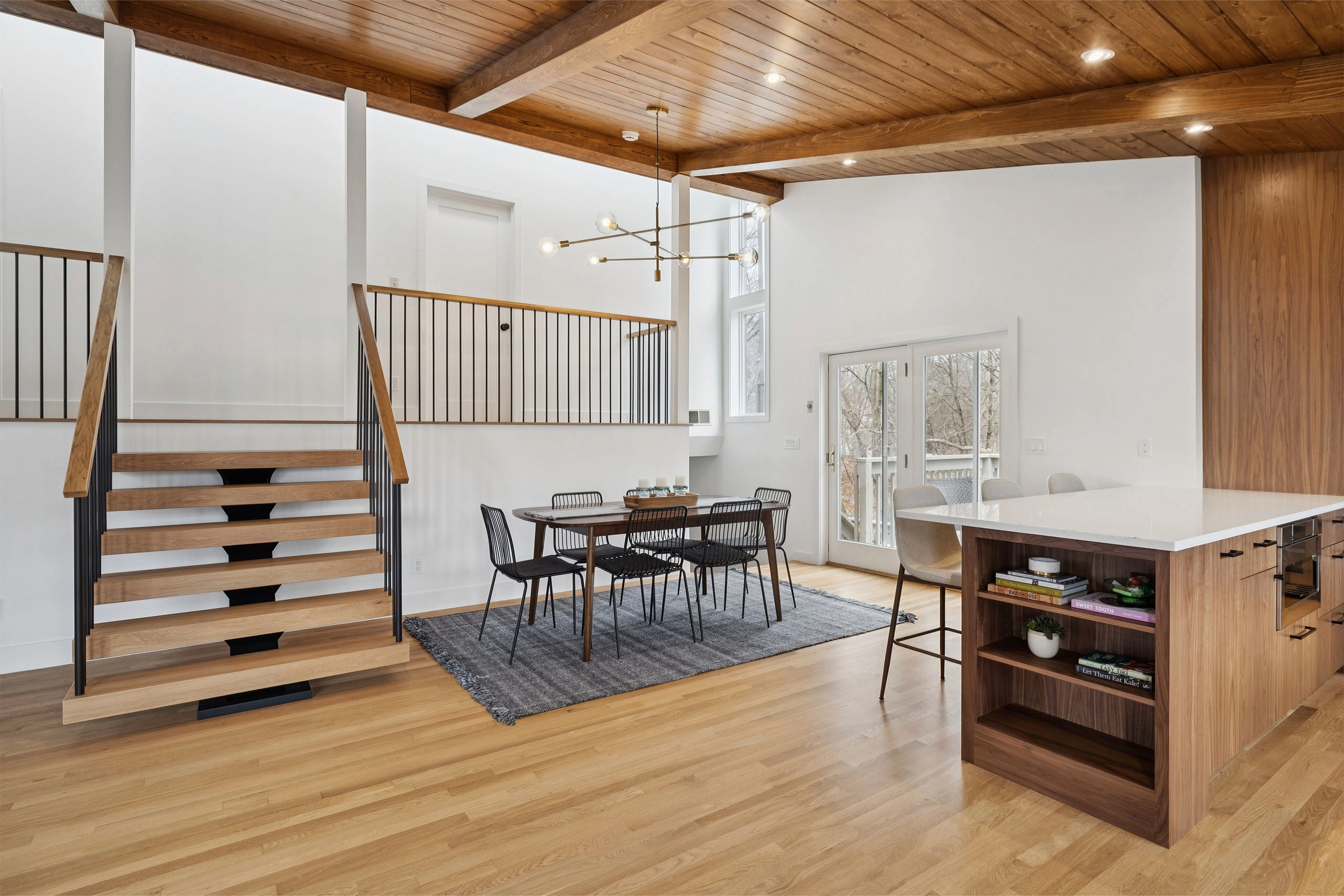 Open dining area with a wood plank ceiling and a floating stair rising at left