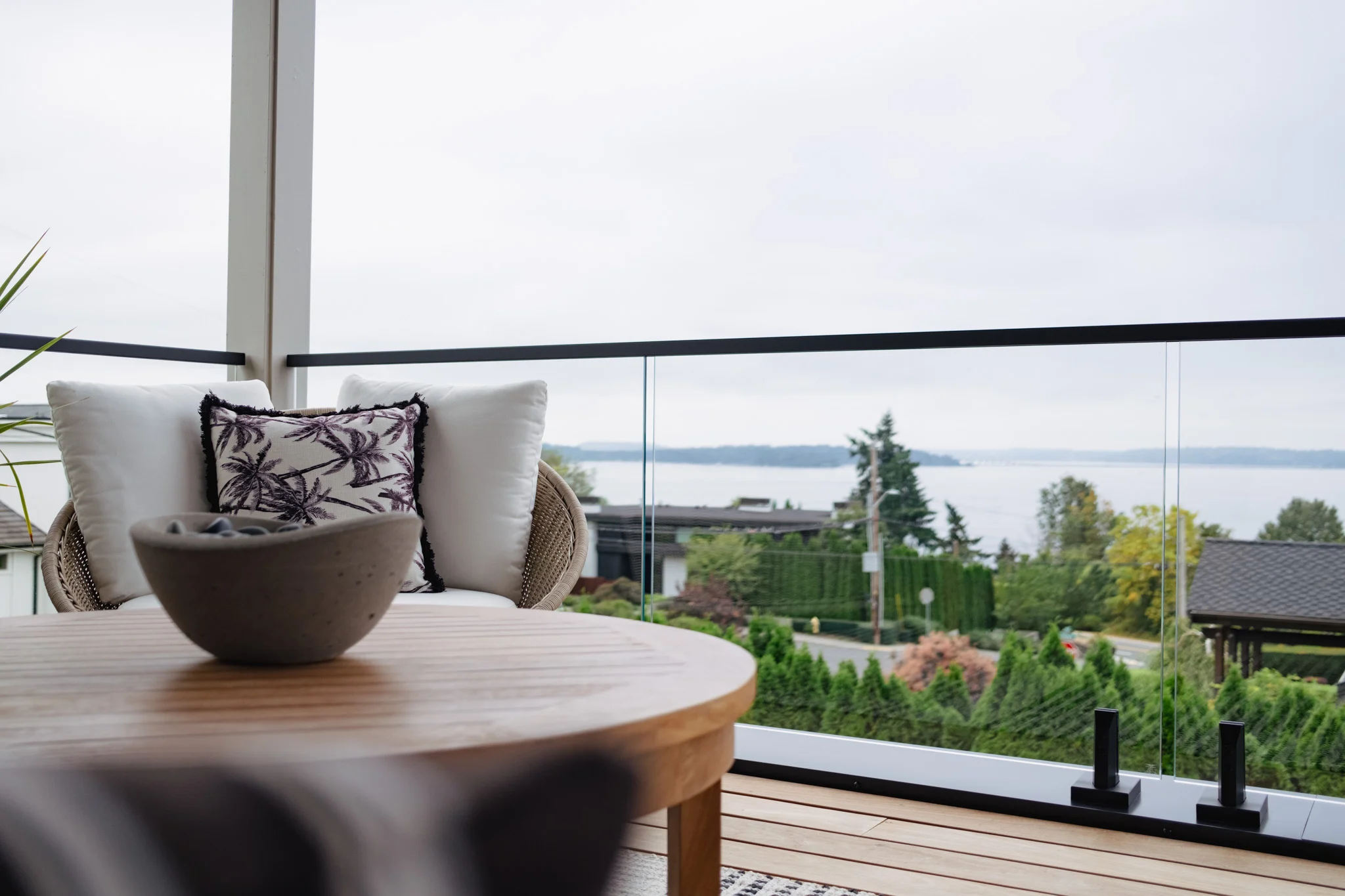 Covered deck seating with glass railing framing an open water view beyond the table