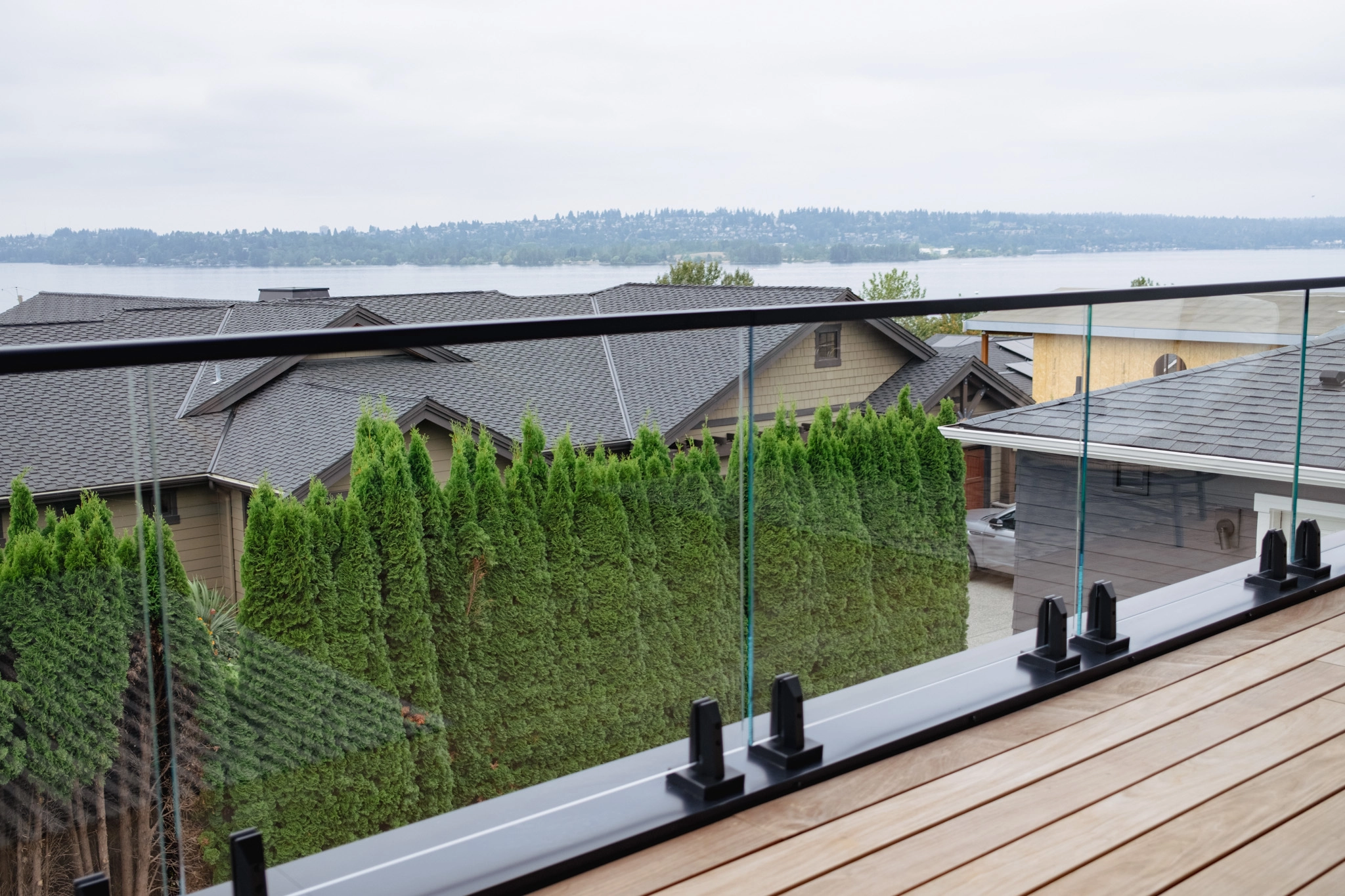 Glass railing on black clamps runs along the deck above hedges and lake