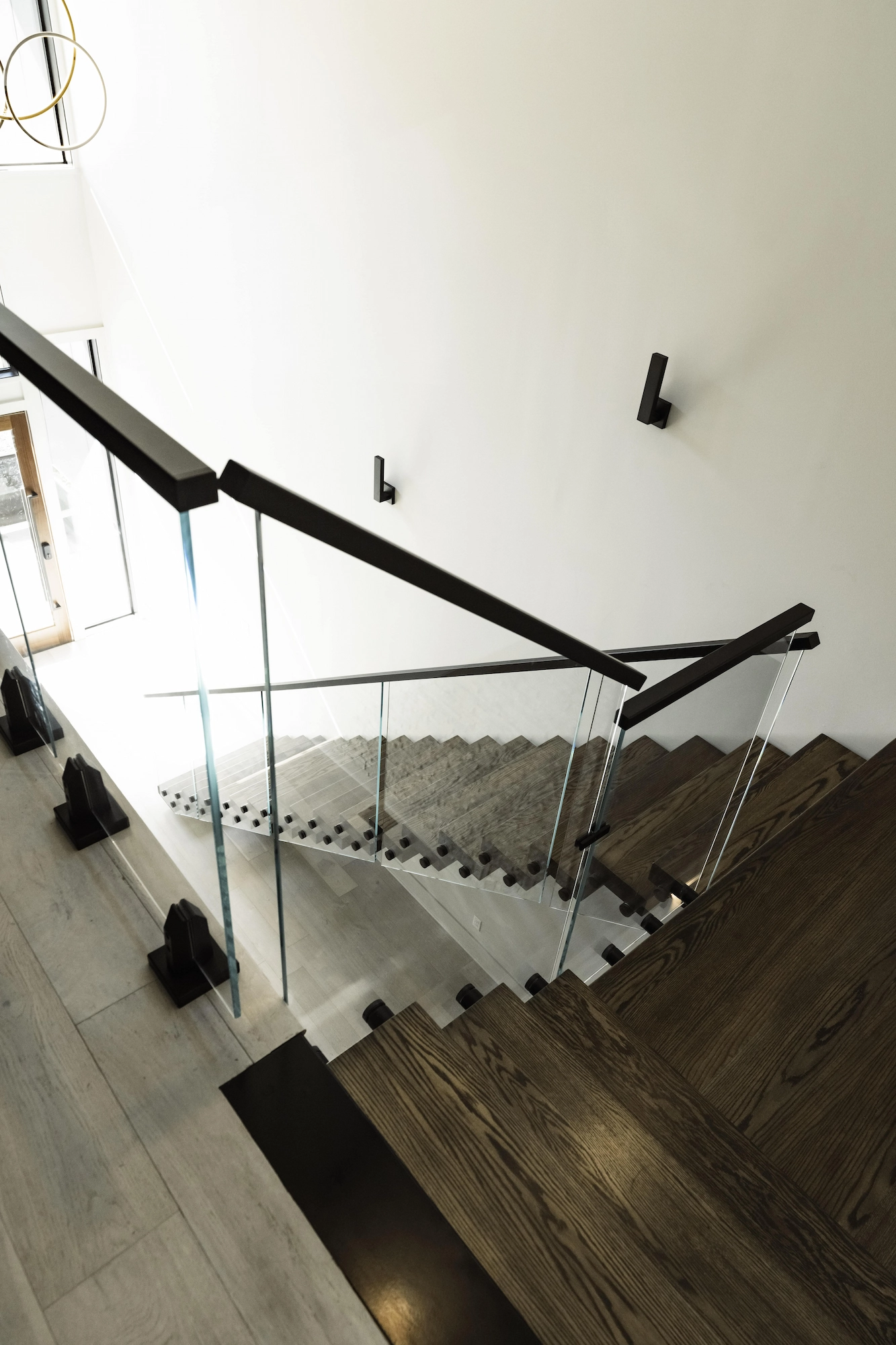 Looking down the stairwell at glass panels and a black handrail over wood floors